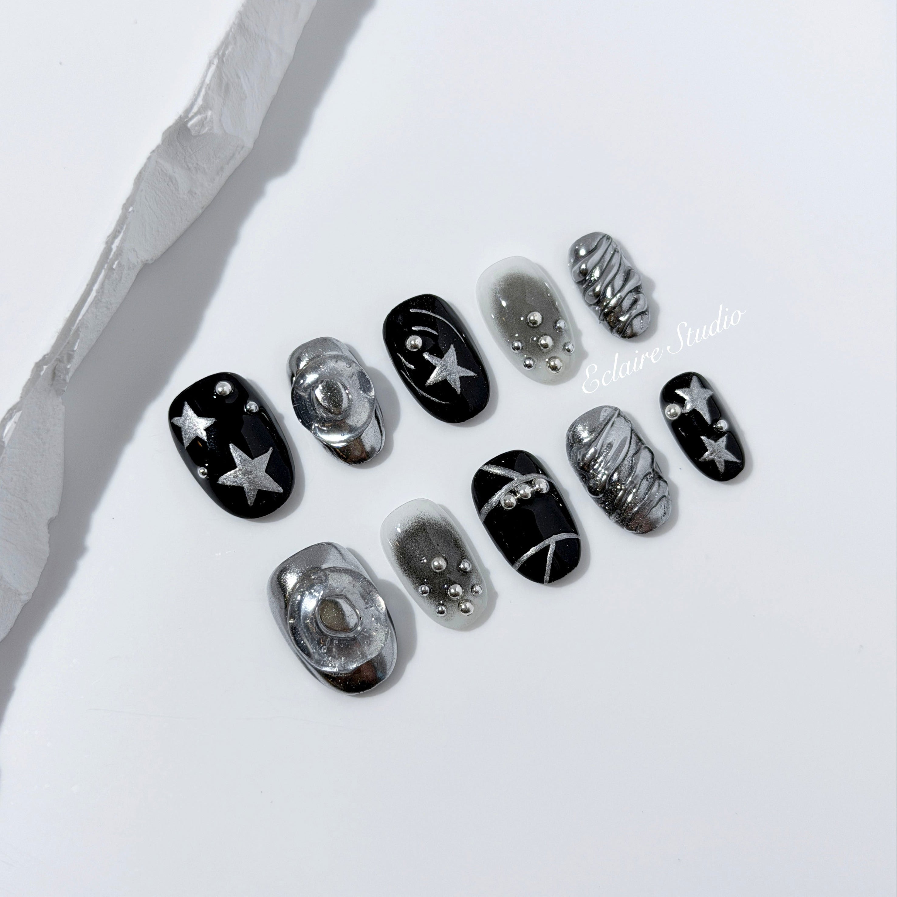 Black and silver press-on nails with 3D chrome swirl accents, star details, and shimmer gradient in a bold winter aesthetic.