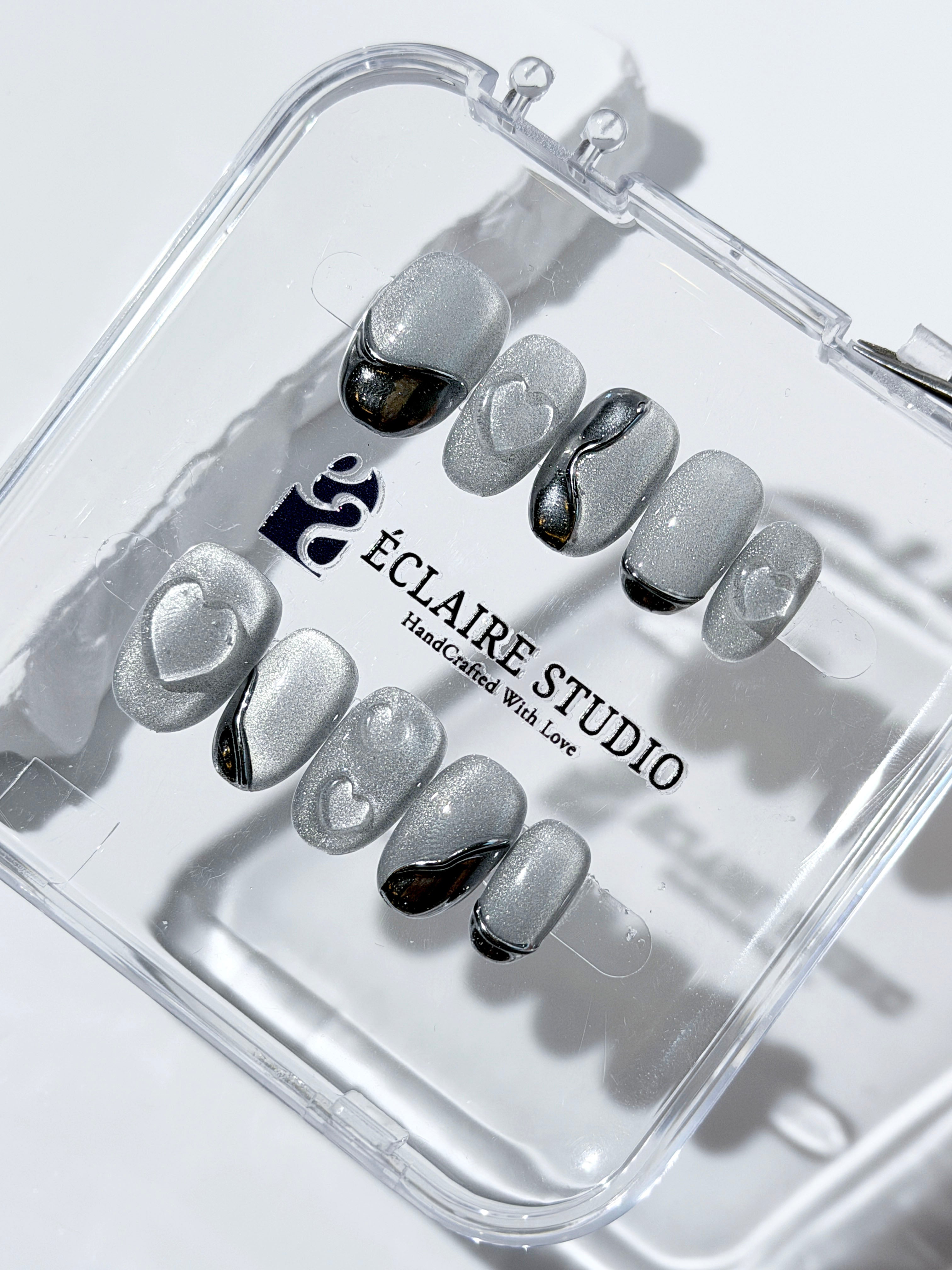 Extra short silver cat-eye press-on nails with chrome ripple accents and 3D heart details, minimalist winter aesthetic.