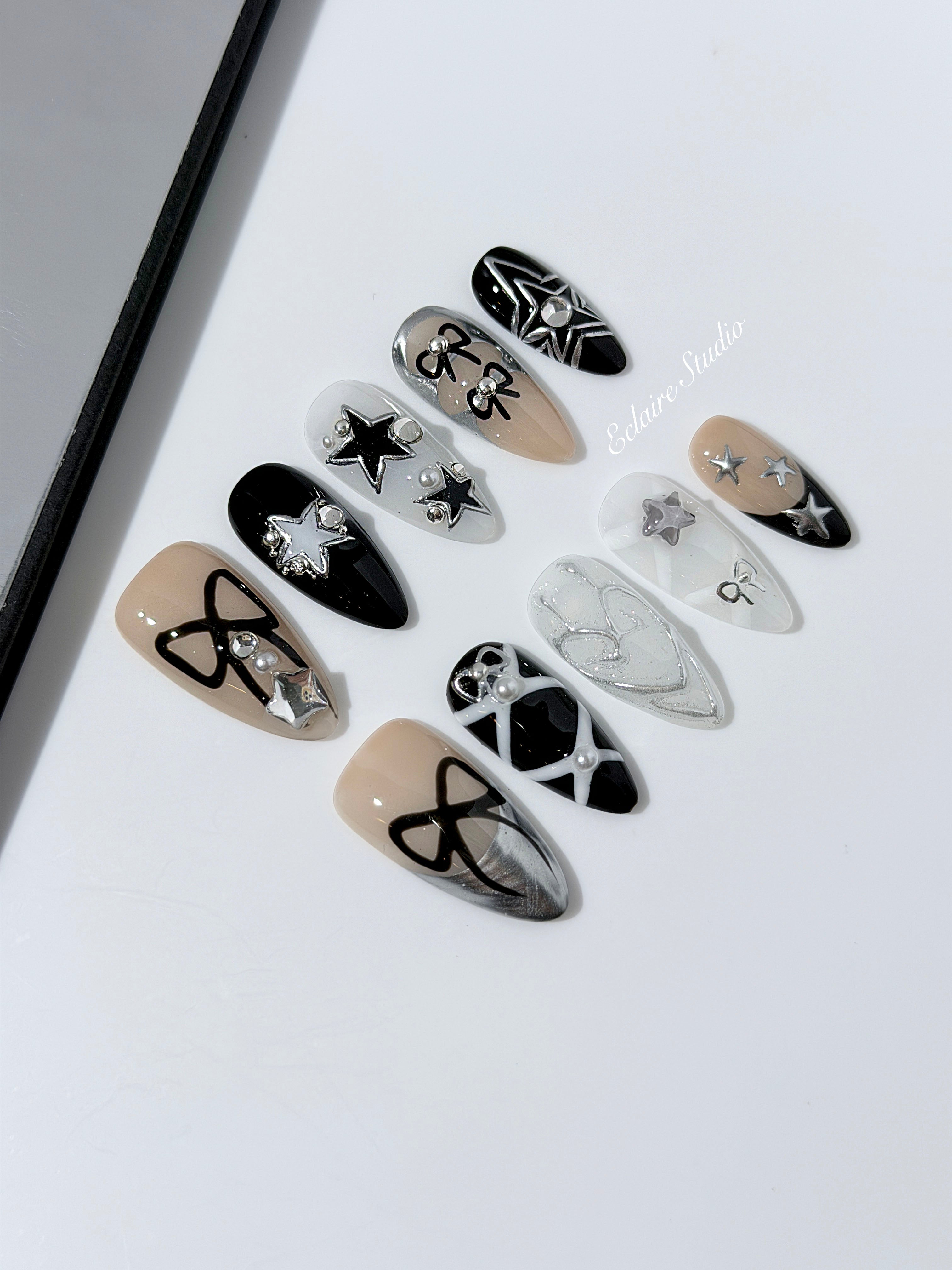 Handmade black, white, and nude press-on nails featuring bows, star charms, and pearl embellishments.