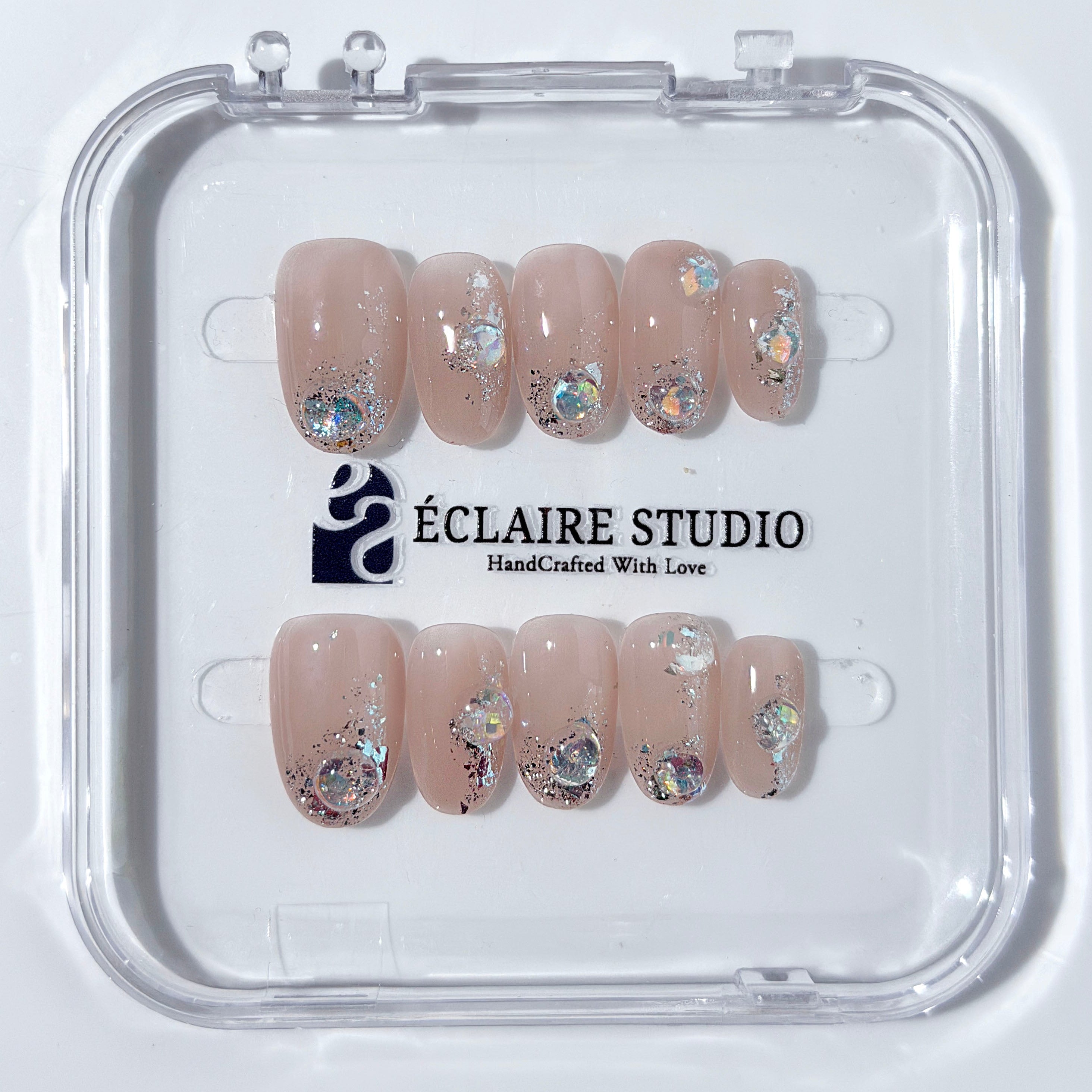 Short milky nude press-on nails with iridescent glitter and 3D crystal droplets, soft winter sugar aesthetic.