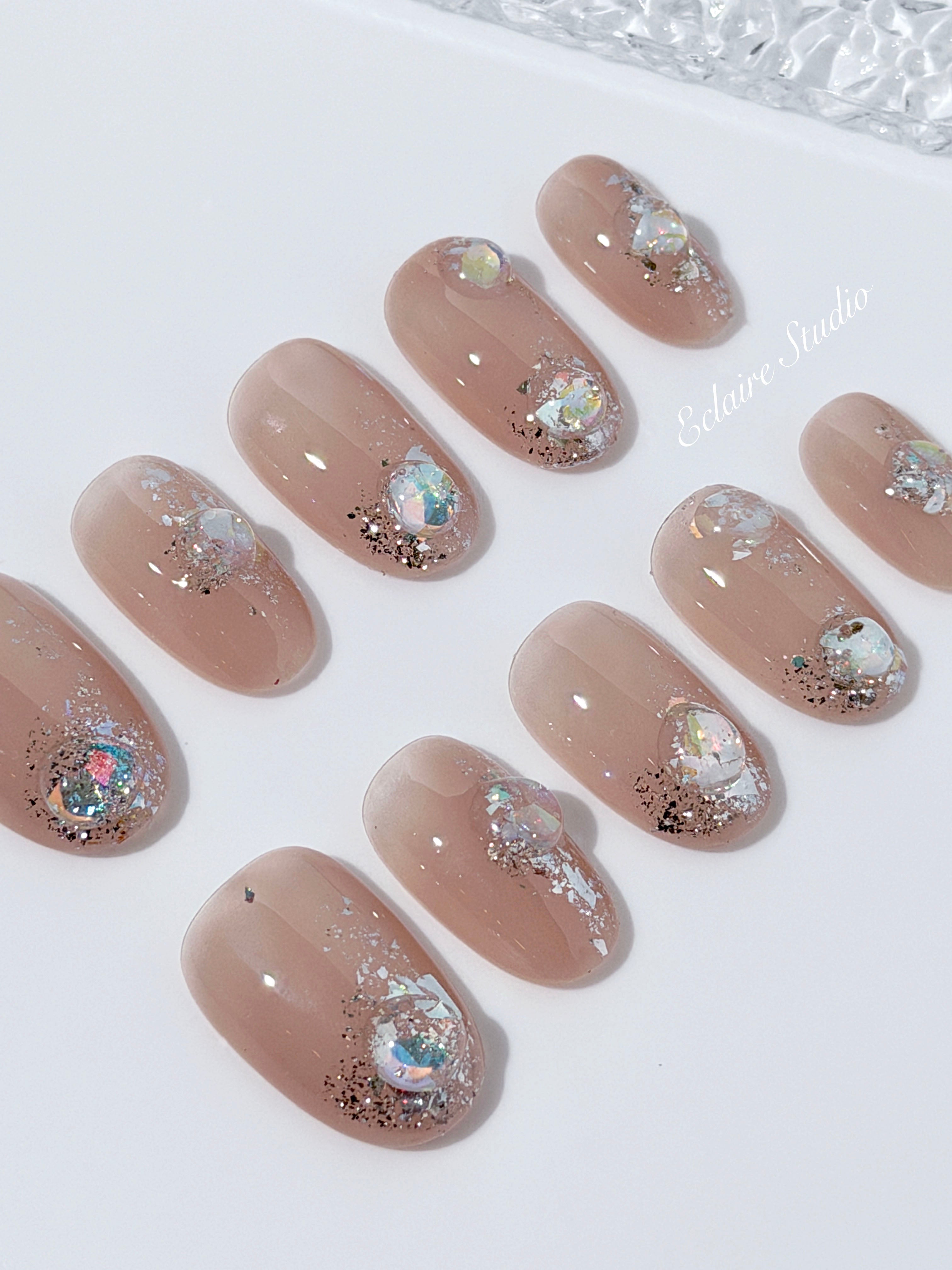 Short milky nude press-on nails with iridescent glitter and 3D crystal droplets, soft winter sugar aesthetic.
