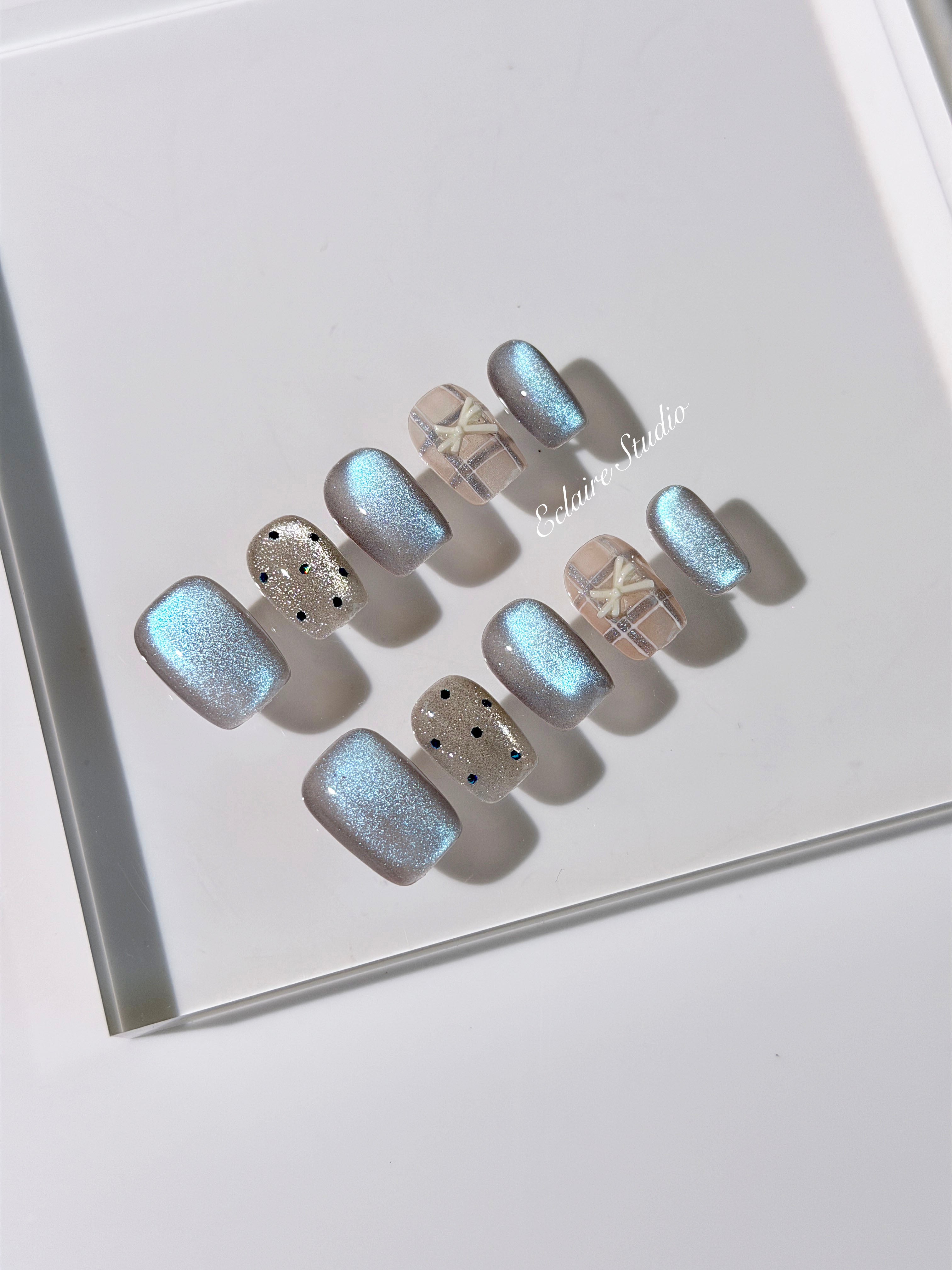 Pastel blue cat-eye press-on nails with glitter accents and 3D clear star details in a soft winter sorbet aesthetic.