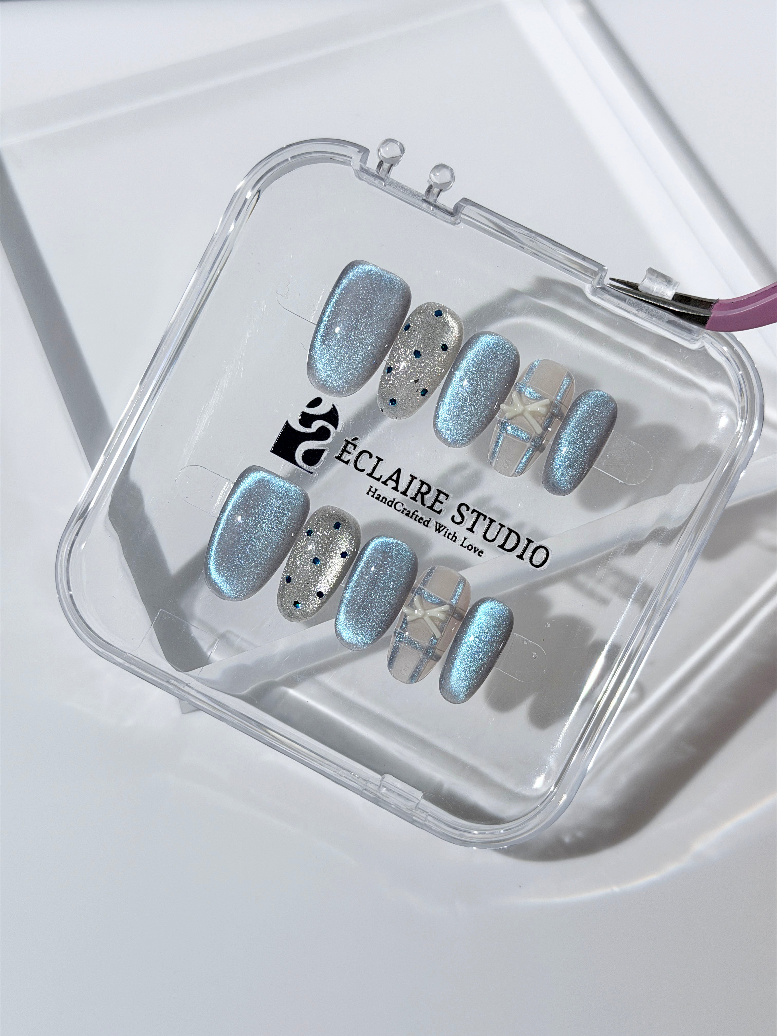 Pastel blue cat-eye press-on nails with glitter accents and 3D clear star details in a soft winter sorbet aesthetic.