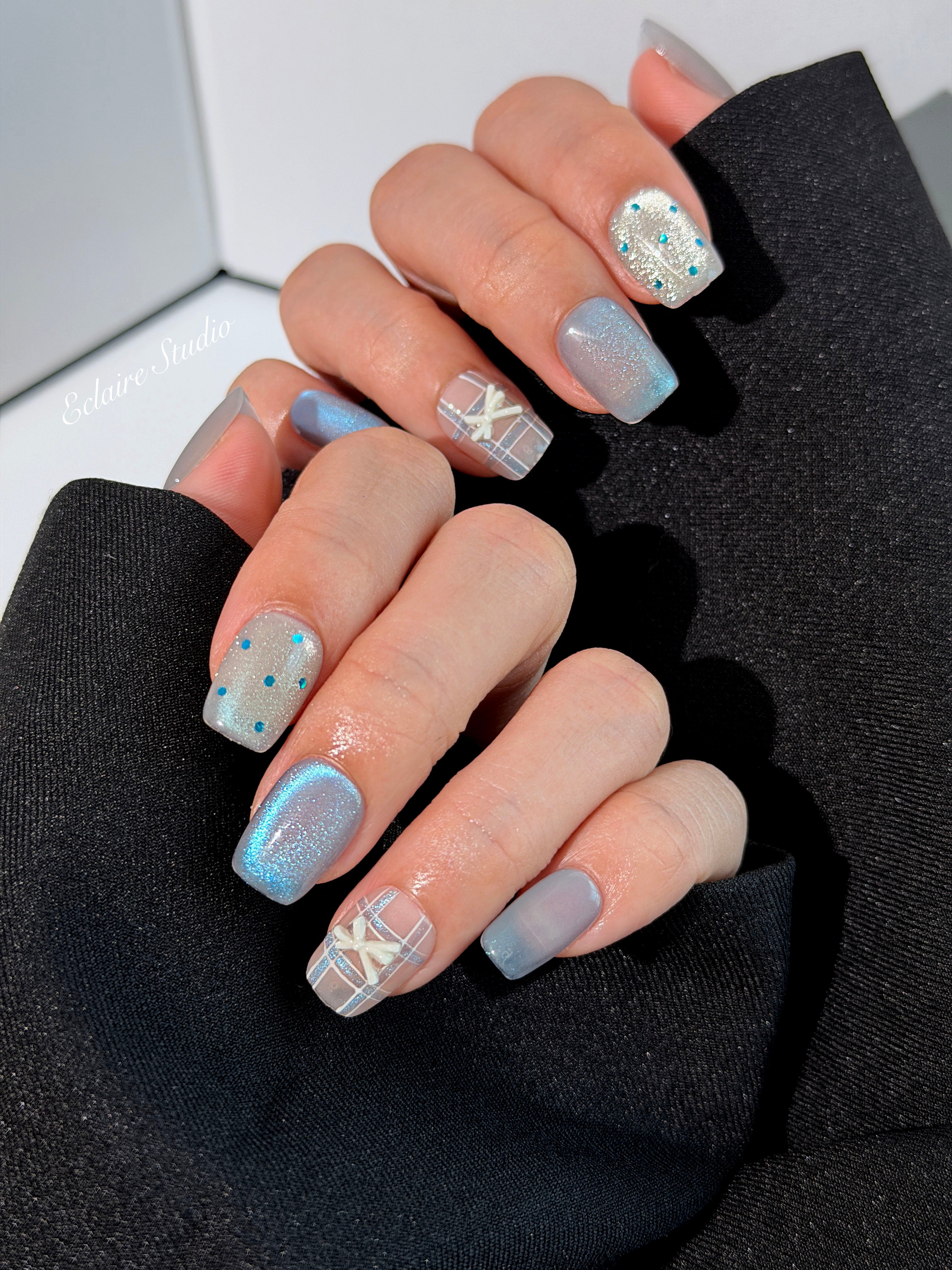 Pastel blue cat-eye press-on nails with glitter accents and 3D clear star details in a soft winter sorbet aesthetic.