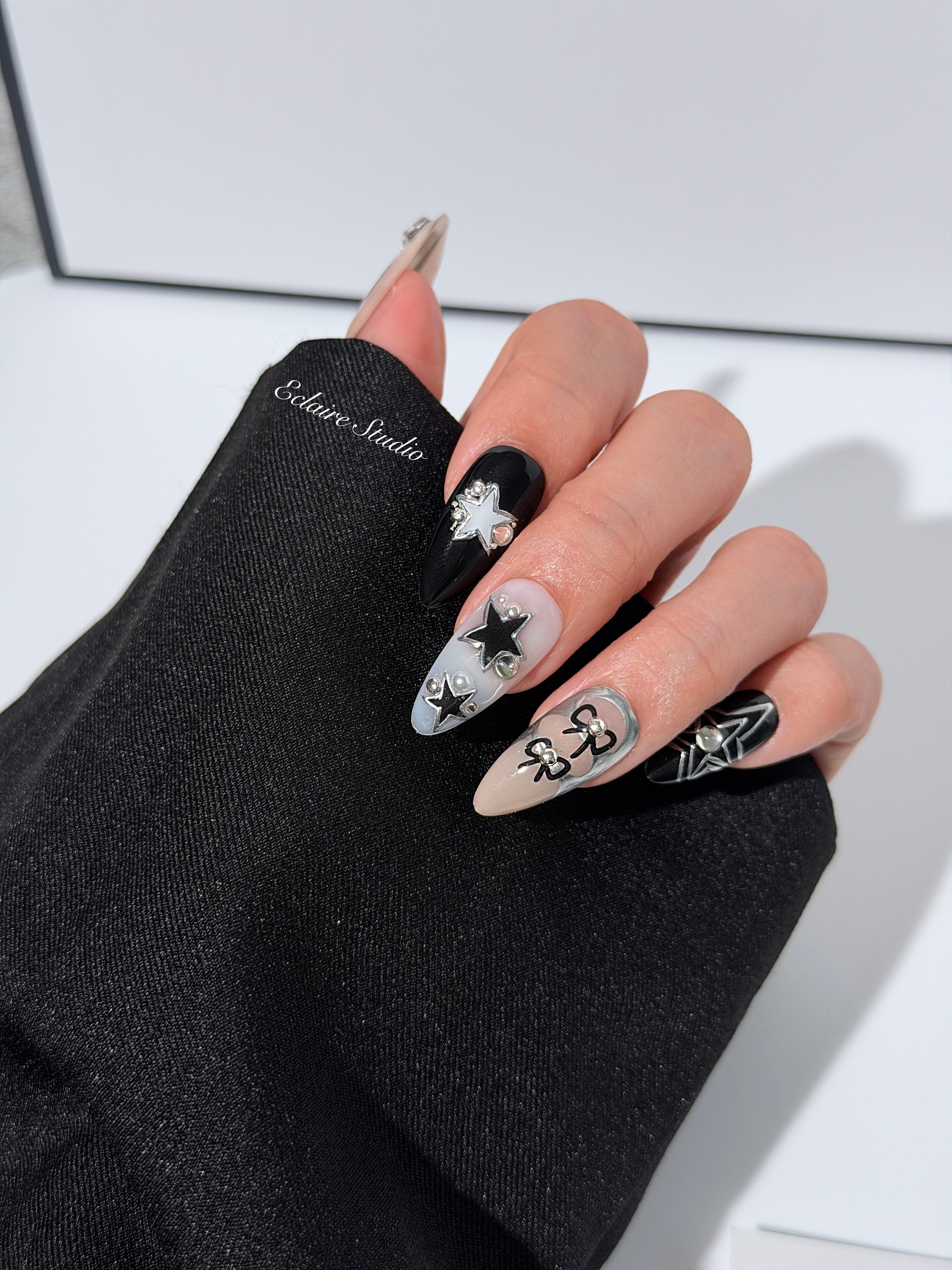 Handmade black, white, and nude press-on nails featuring bows, star charms, and pearl embellishments.