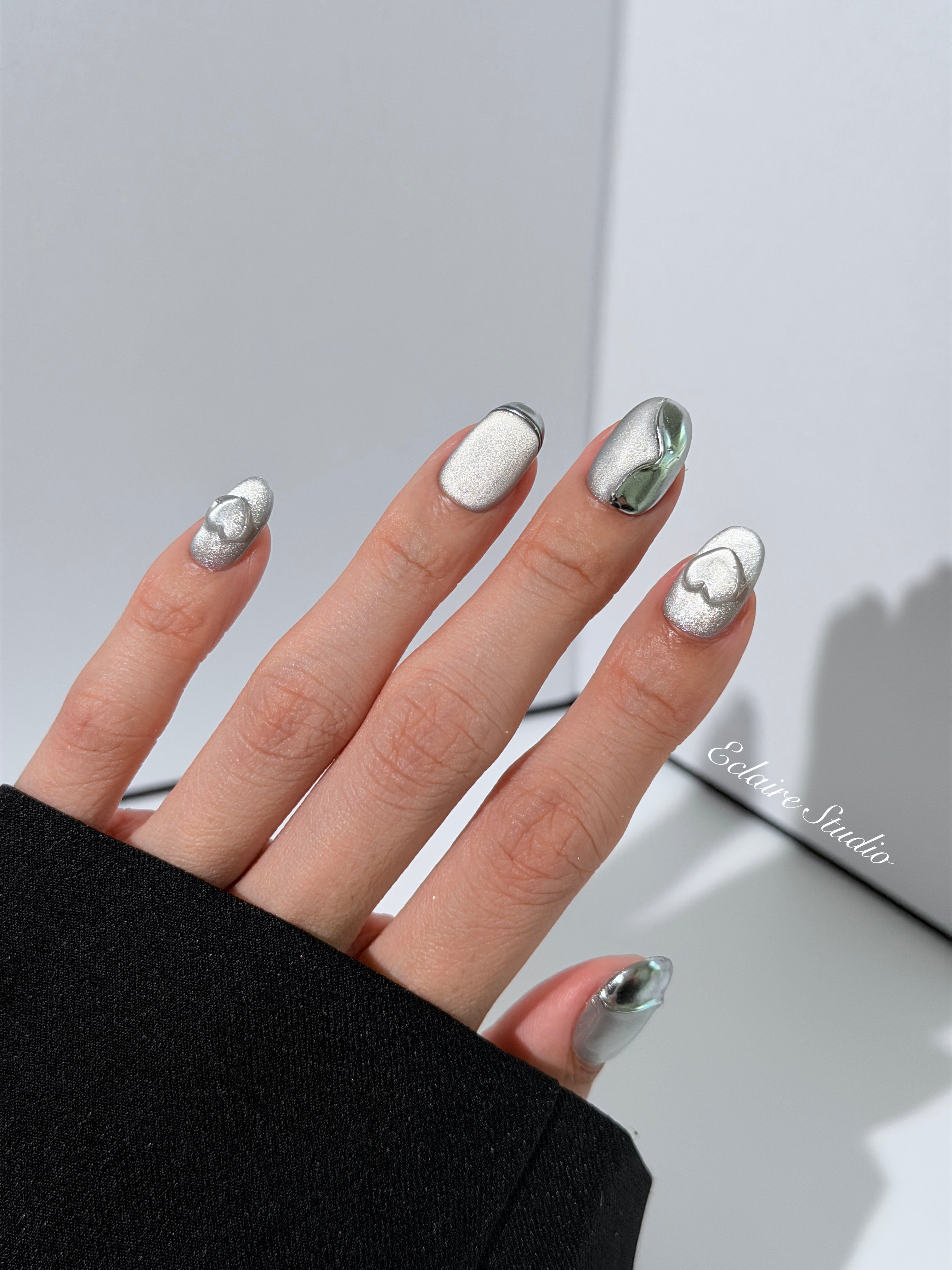 Extra short silver cat-eye press-on nails with chrome ripple accents and 3D heart details, minimalist winter aesthetic.