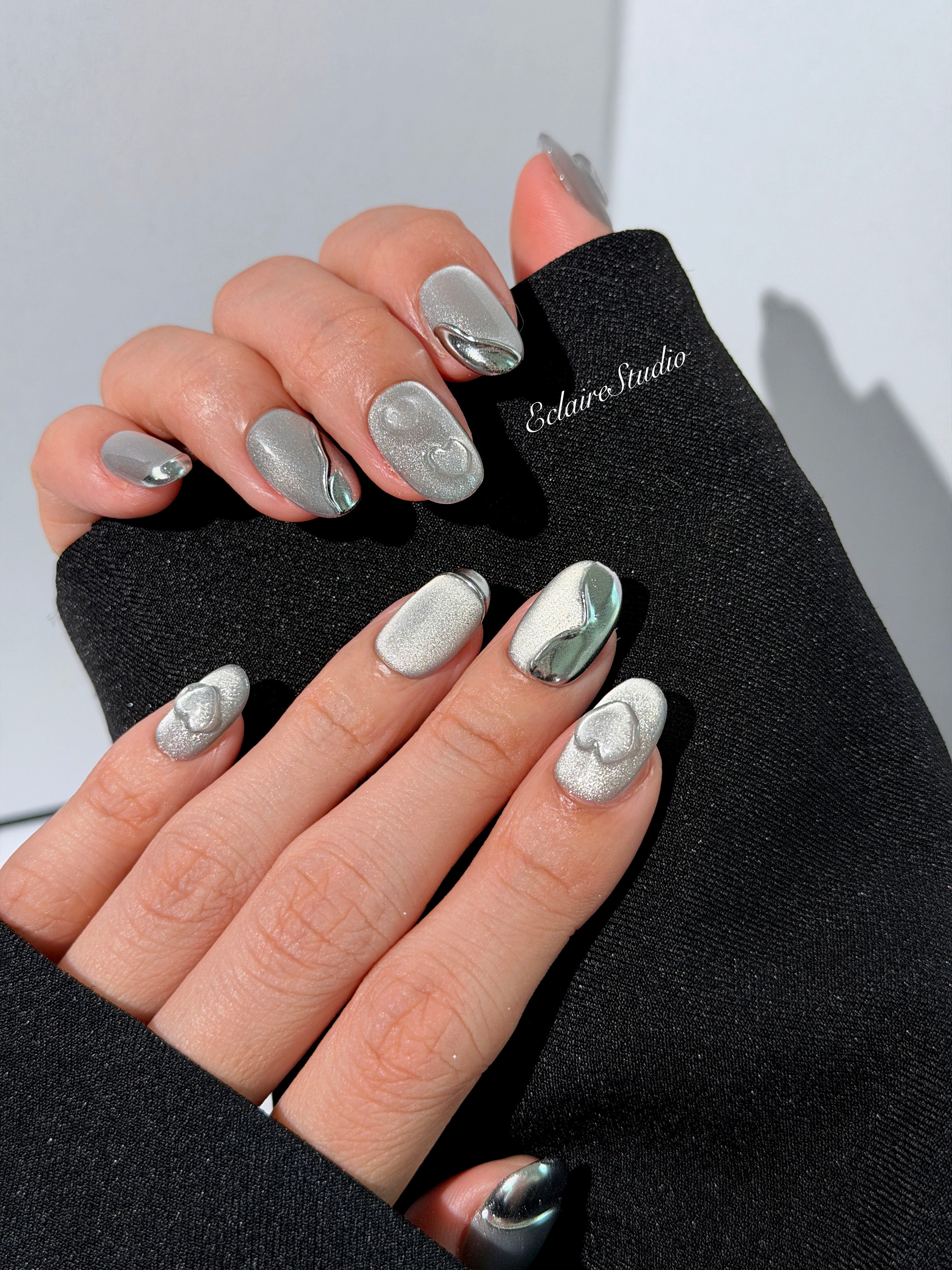 Extra short silver cat-eye press-on nails with chrome ripple accents and 3D heart details, minimalist winter aesthetic.