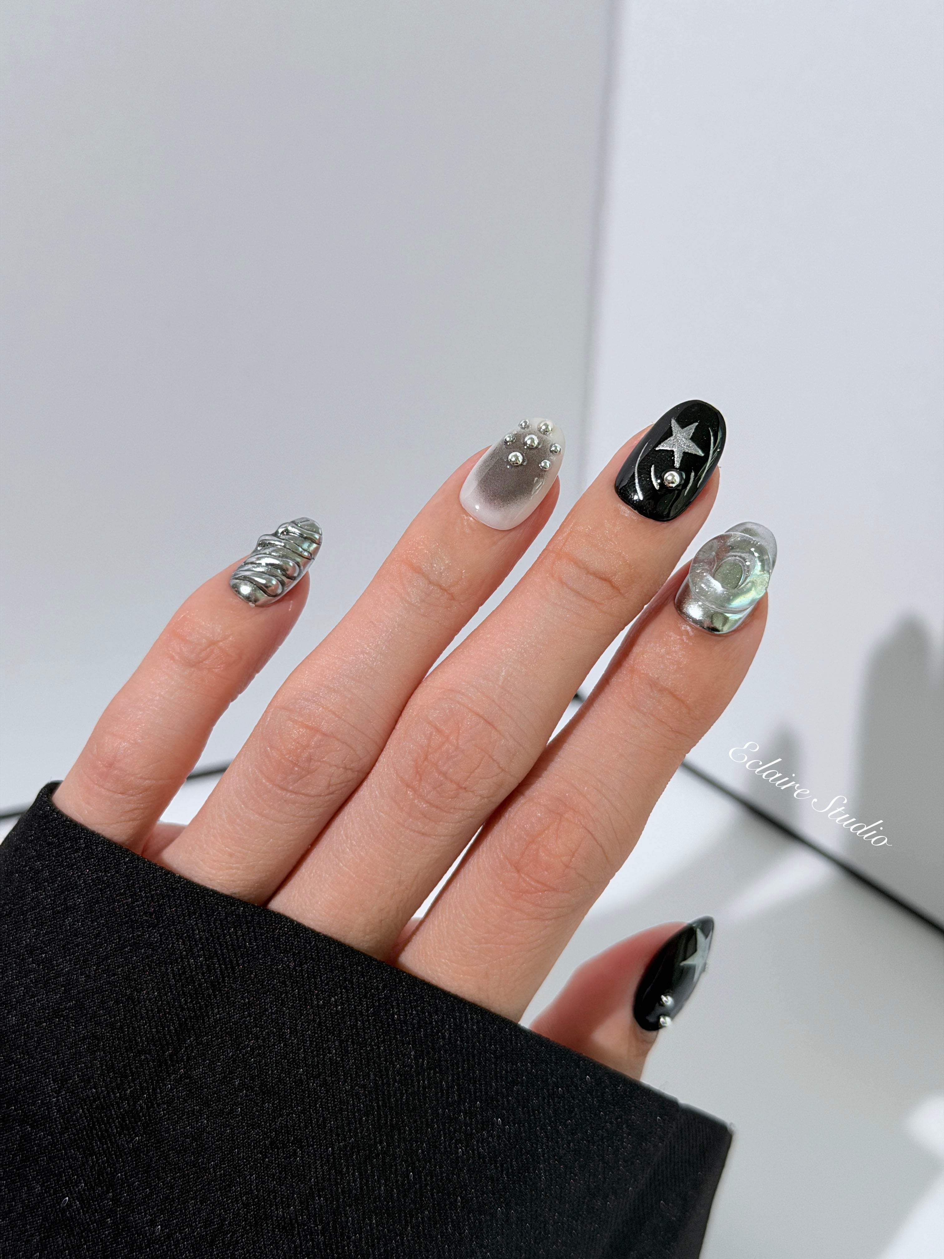 Black and silver press-on nails with 3D chrome swirl accents, star details, and shimmer gradient in a bold winter aesthetic.