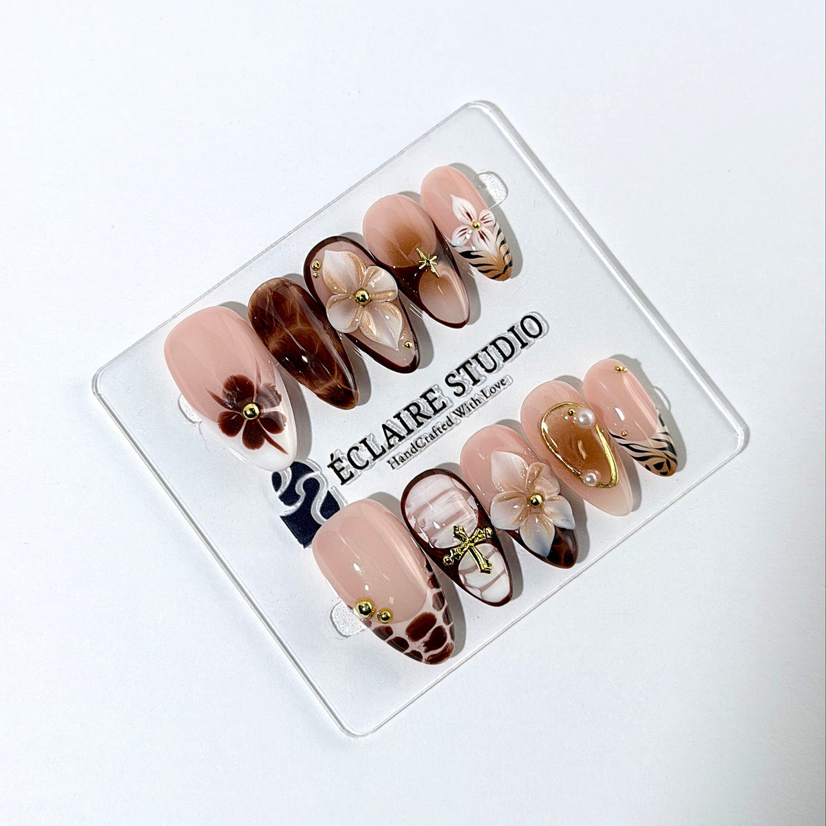 Petal Locket almond press-on nails with nude bases, ivory 3D flowers, brown florals, tortoiseshell, animal-print French tips, pearls, and gold accents.