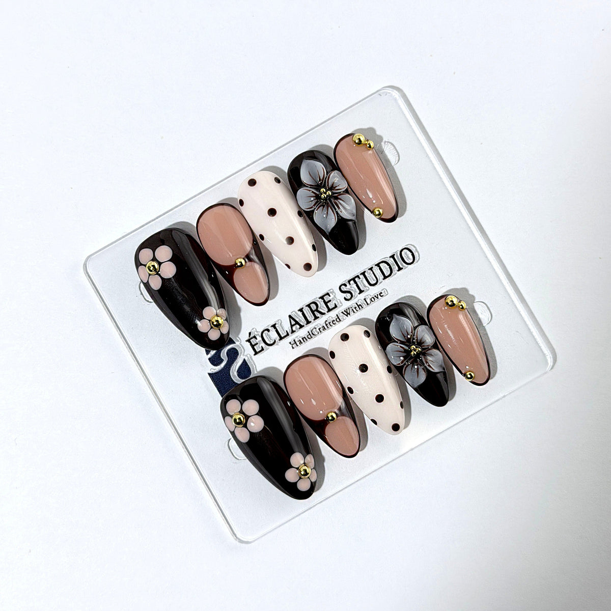 Cocoa Cameo almond press-on nails with espresso and blush bases, brown polka dots on ivory, sculpted flowers, pink daisies, and gold beads.