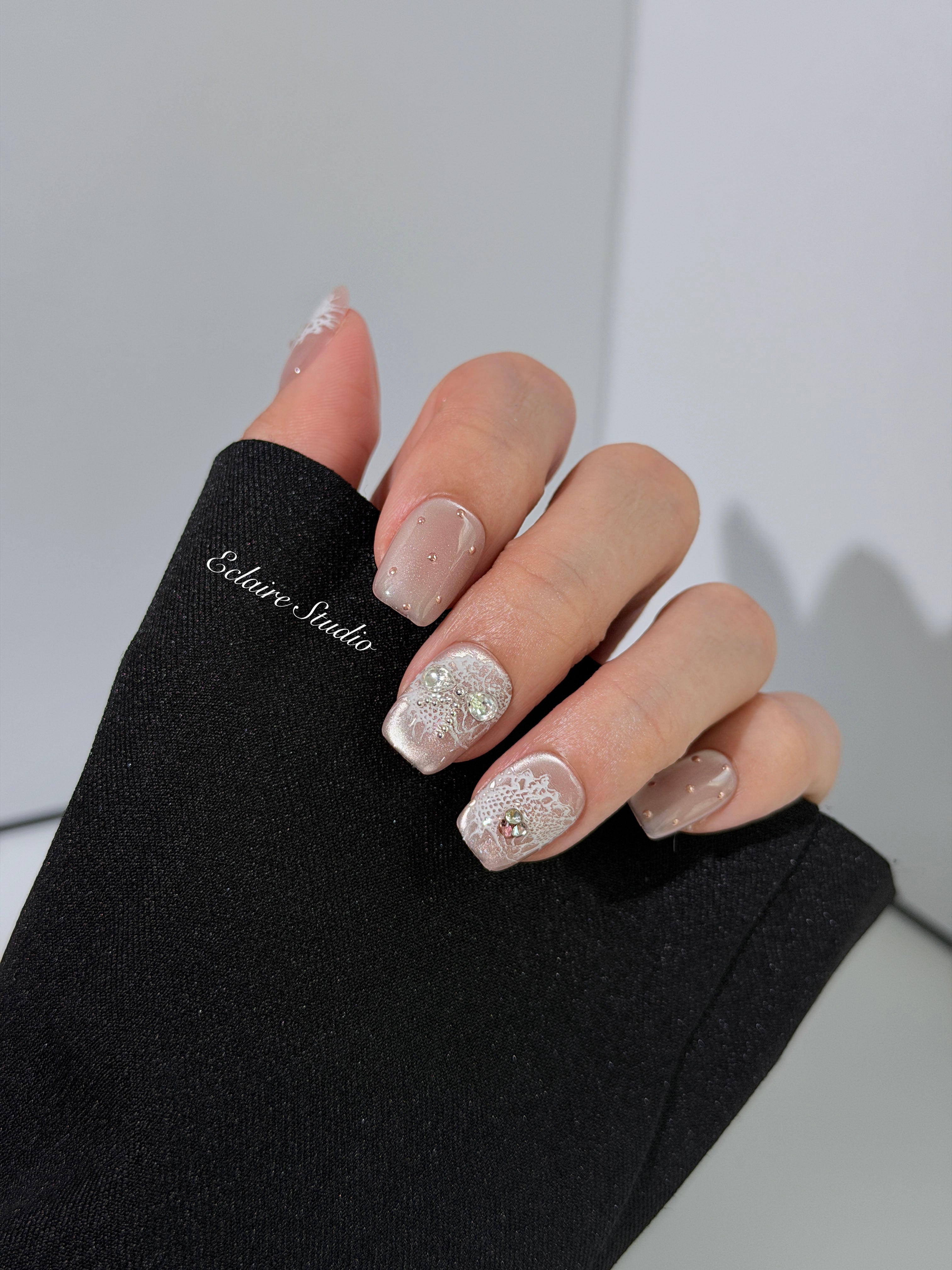 Short coffin pink nude cat-eye press-on nails with lace texture and pearl bow accents in a soft romantic winter style.