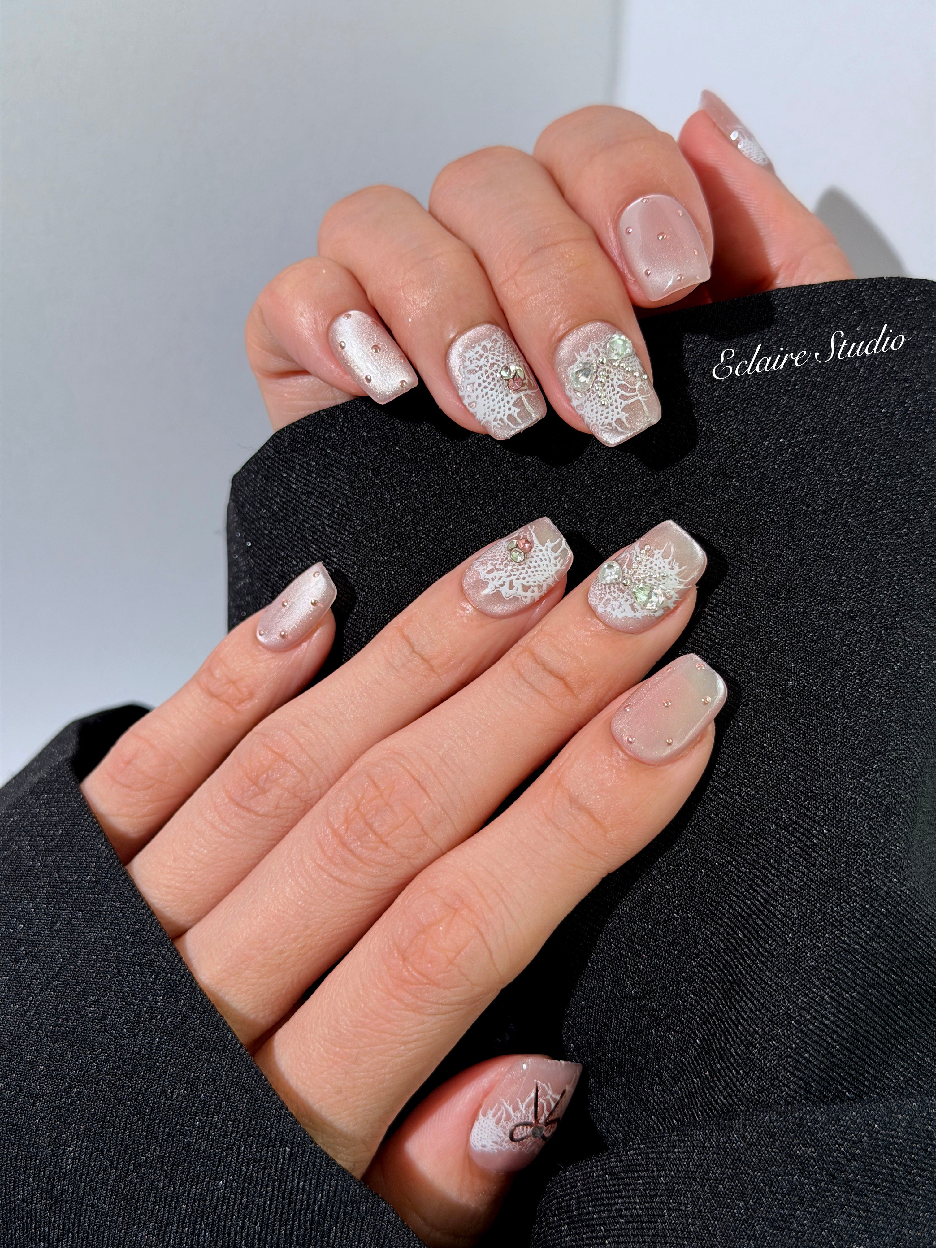 Short coffin pink nude cat-eye press-on nails with lace texture and pearl bow accents in a soft romantic winter style.