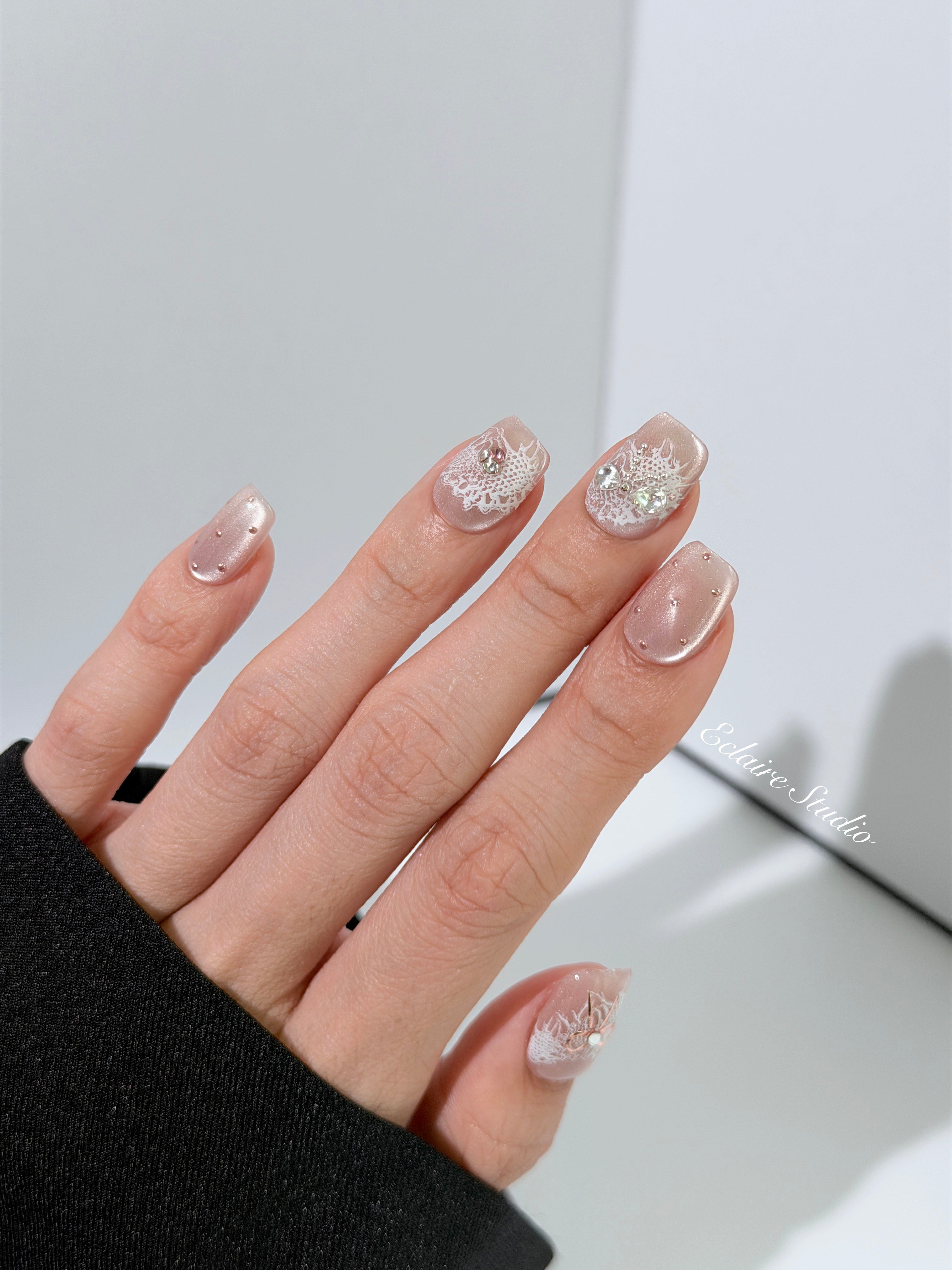 Short coffin pink nude cat-eye press-on nails with lace texture and pearl bow accents in a soft romantic winter style.