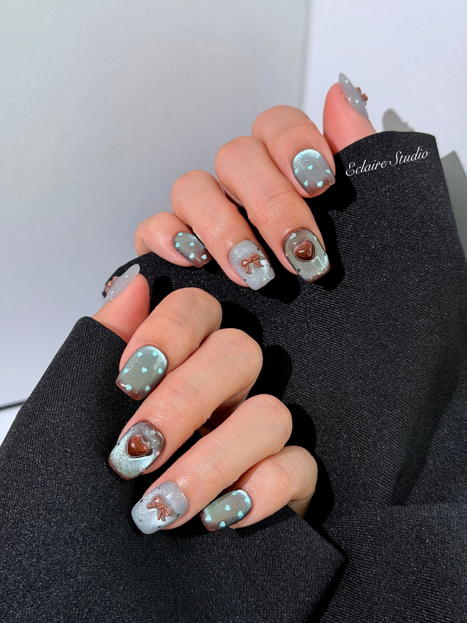 Close-up of short coffin mint shimmer and chocolate brown gradient press-on nails featuring cute hearts, bows, and glitter accents.