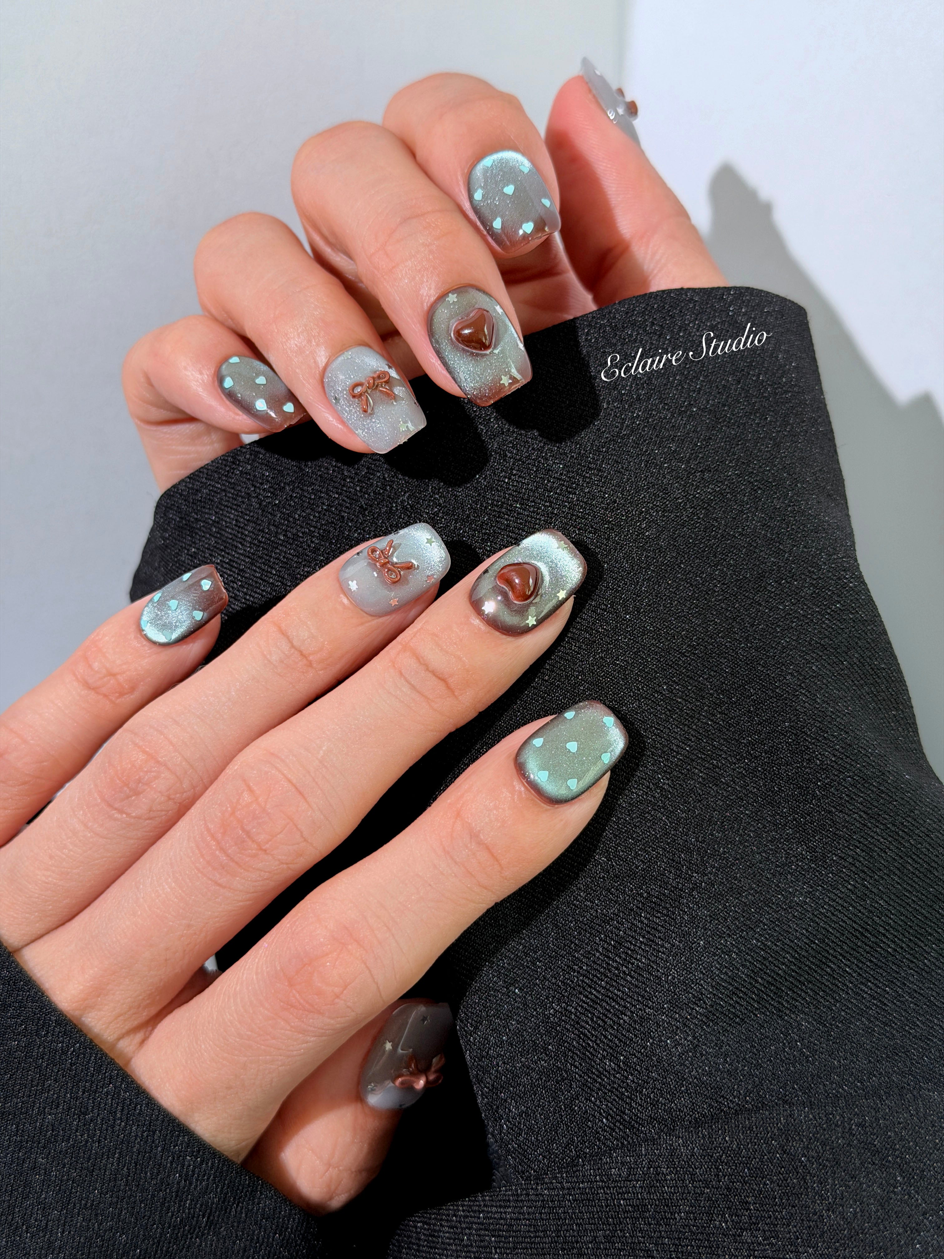 Close-up of short coffin mint shimmer and chocolate brown gradient press-on nails featuring cute hearts, bows, and glitter accents.