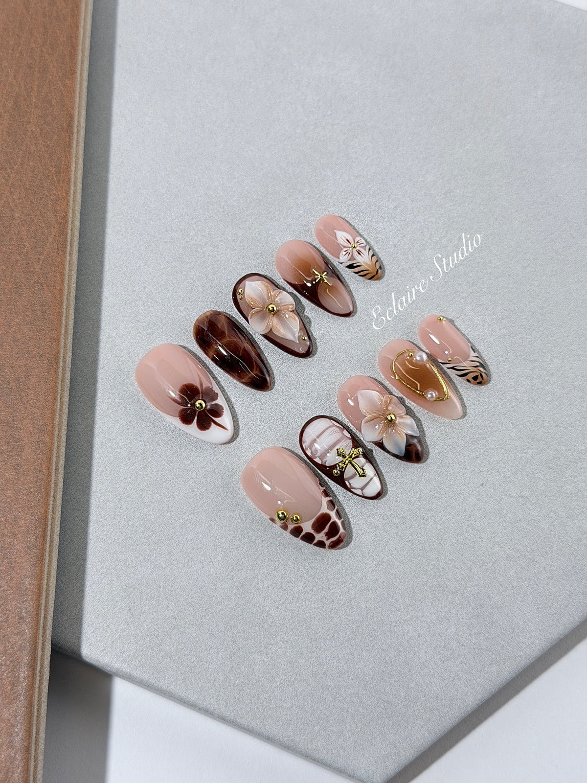 Petal Locket almond press-on nails with nude bases, ivory 3D flowers, brown florals, tortoiseshell, animal-print French tips, pearls, and gold accents.