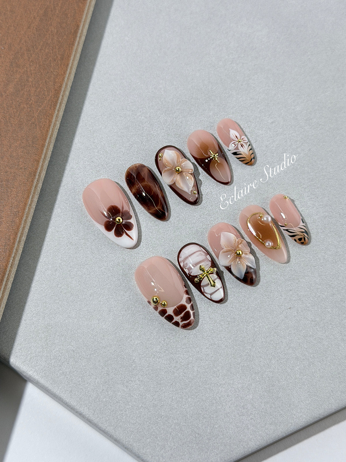 Petal Locket almond press-on nails with nude bases, ivory 3D flowers, brown florals, tortoiseshell, animal-print French tips, pearls, and gold accents.