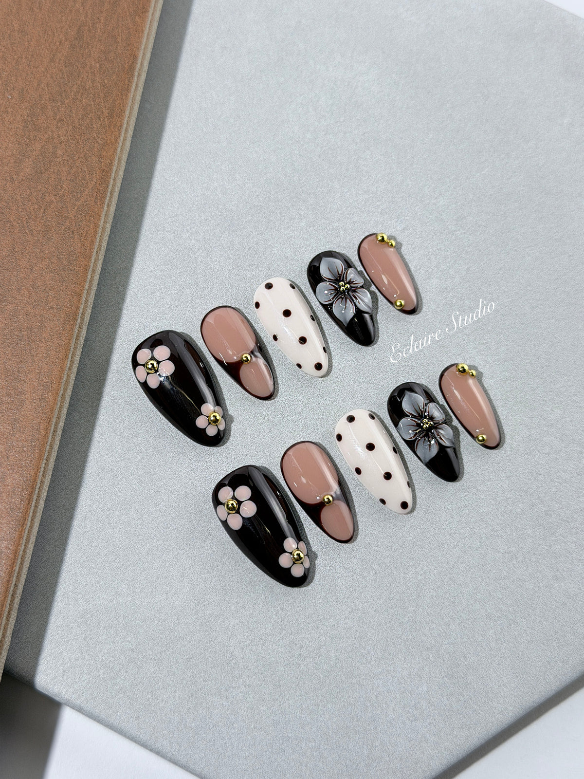 Cocoa Cameo almond press-on nails with espresso and blush bases, brown polka dots on ivory, sculpted flowers, pink daisies, and gold beads.