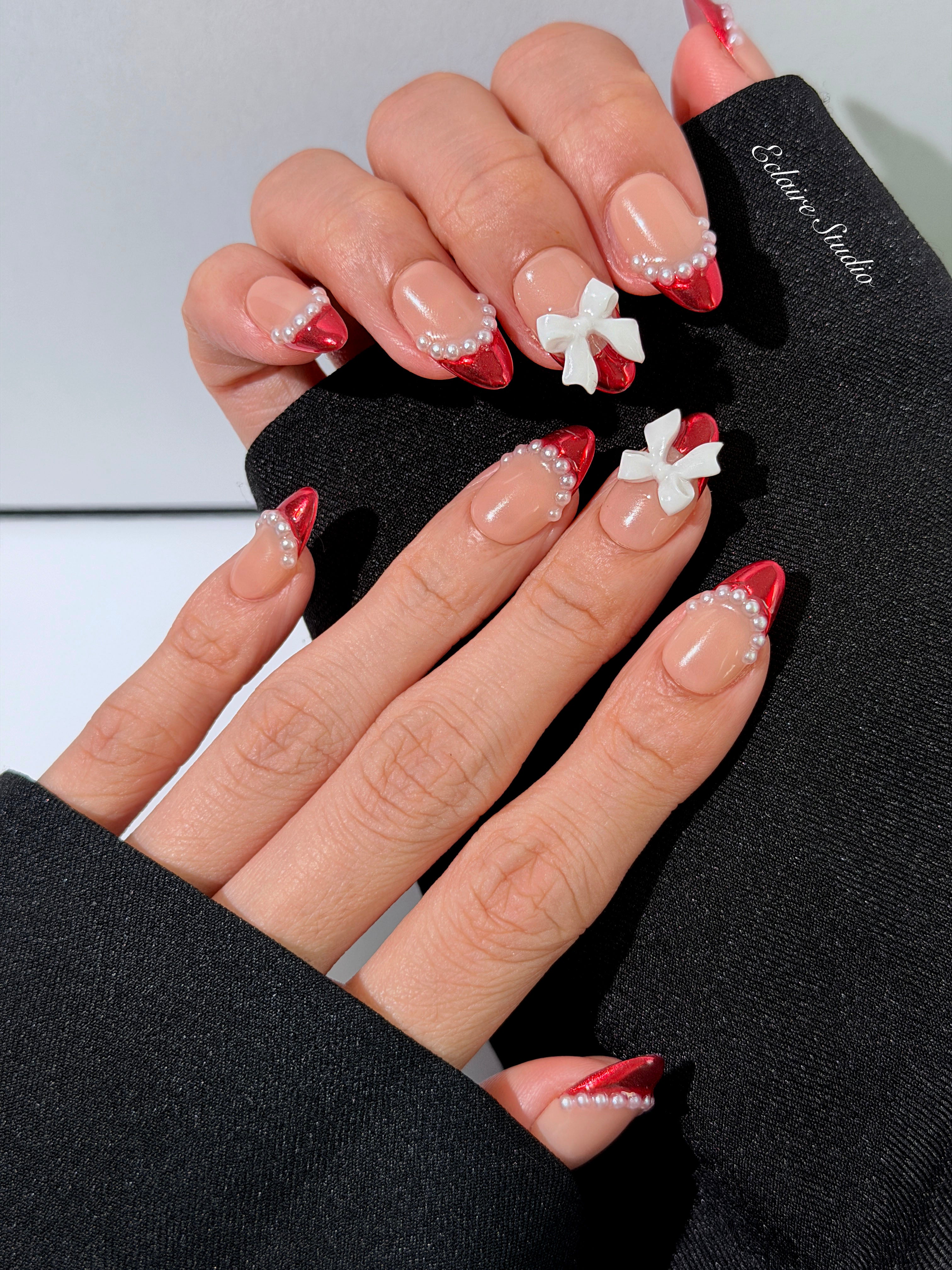 Red Ribbon press-on nails with glazed red chrome French tips, pearl trim, and 3D white bow accents.”
