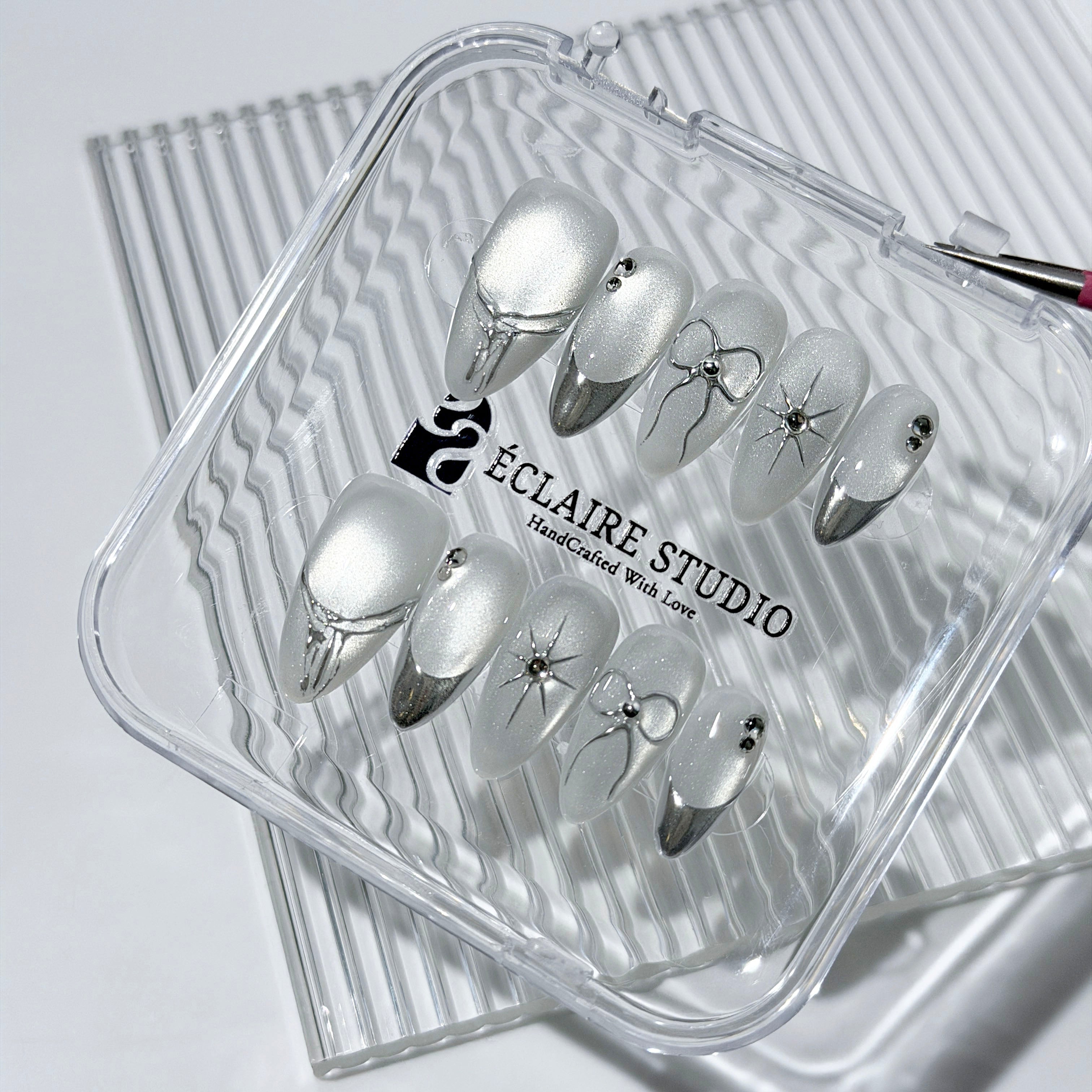 Silver cat-eye press-on nails featuring glazed chrome French tips and fine-line bow and starburst designs.