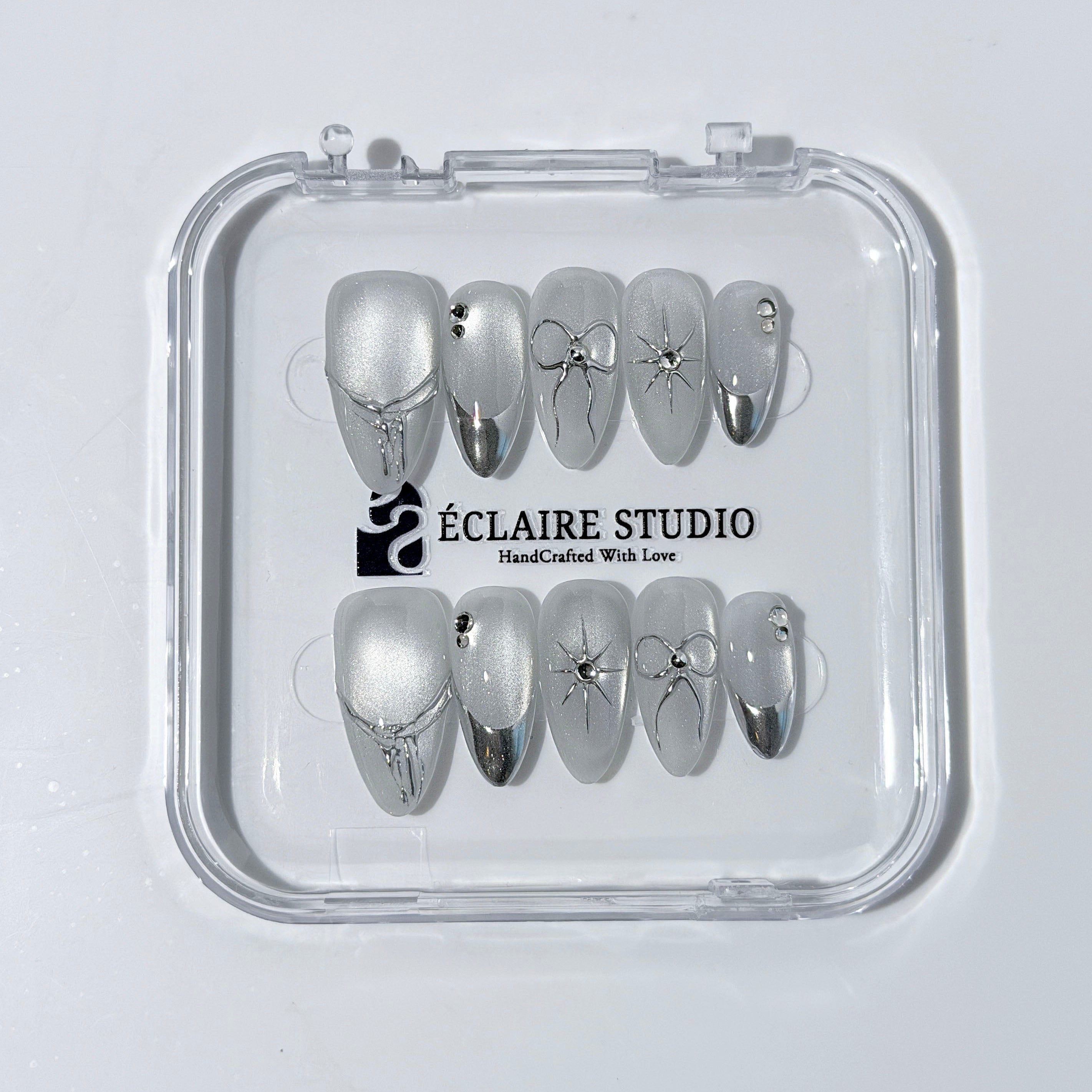 Silver cat-eye press-on nails featuring glazed chrome French tips and fine-line bow and starburst designs.