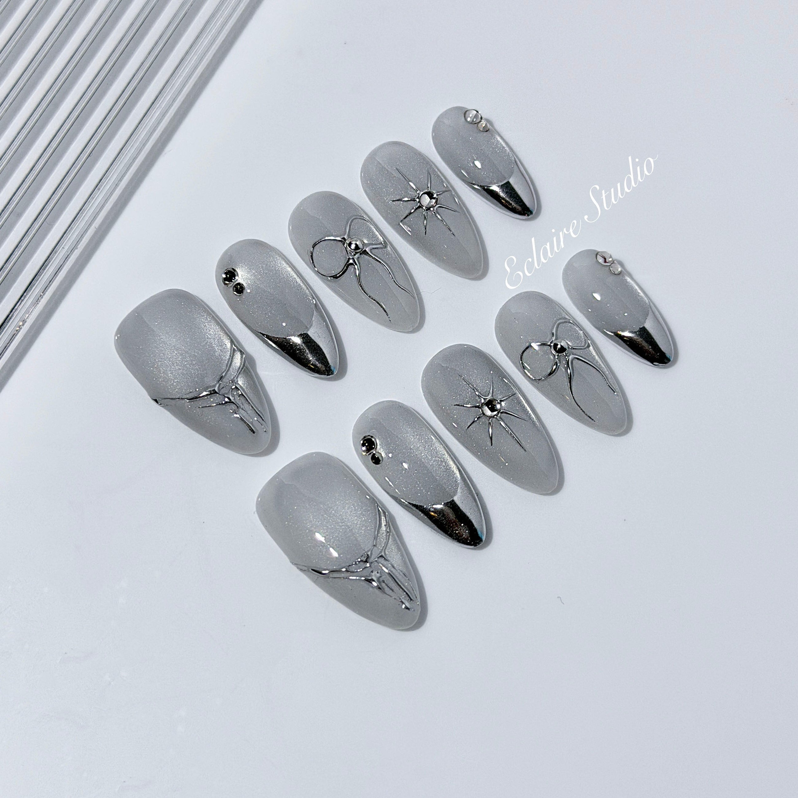 Silver cat-eye press-on nails featuring glazed chrome French tips and fine-line bow and starburst designs.