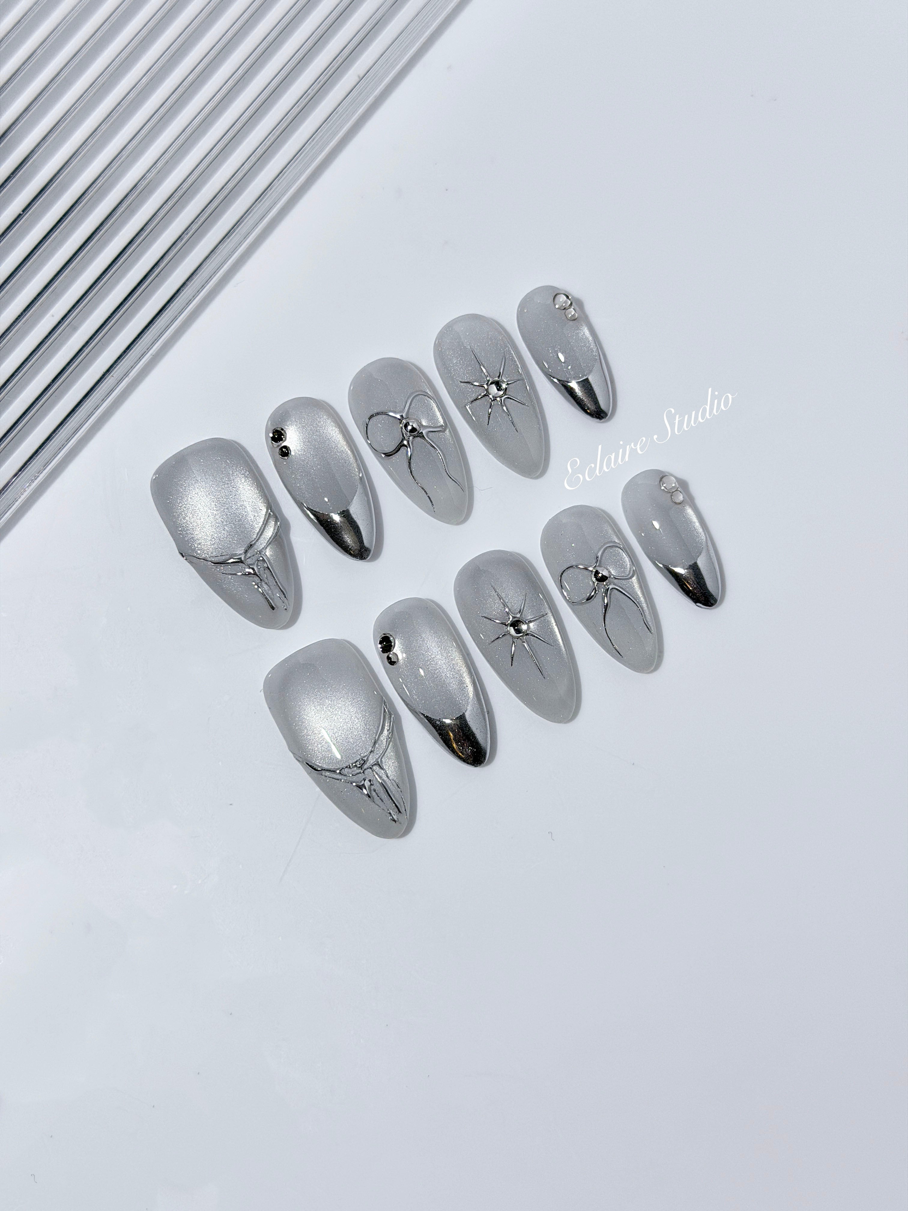 Silver cat-eye press-on nails featuring glazed chrome French tips and fine-line bow and starburst designs.