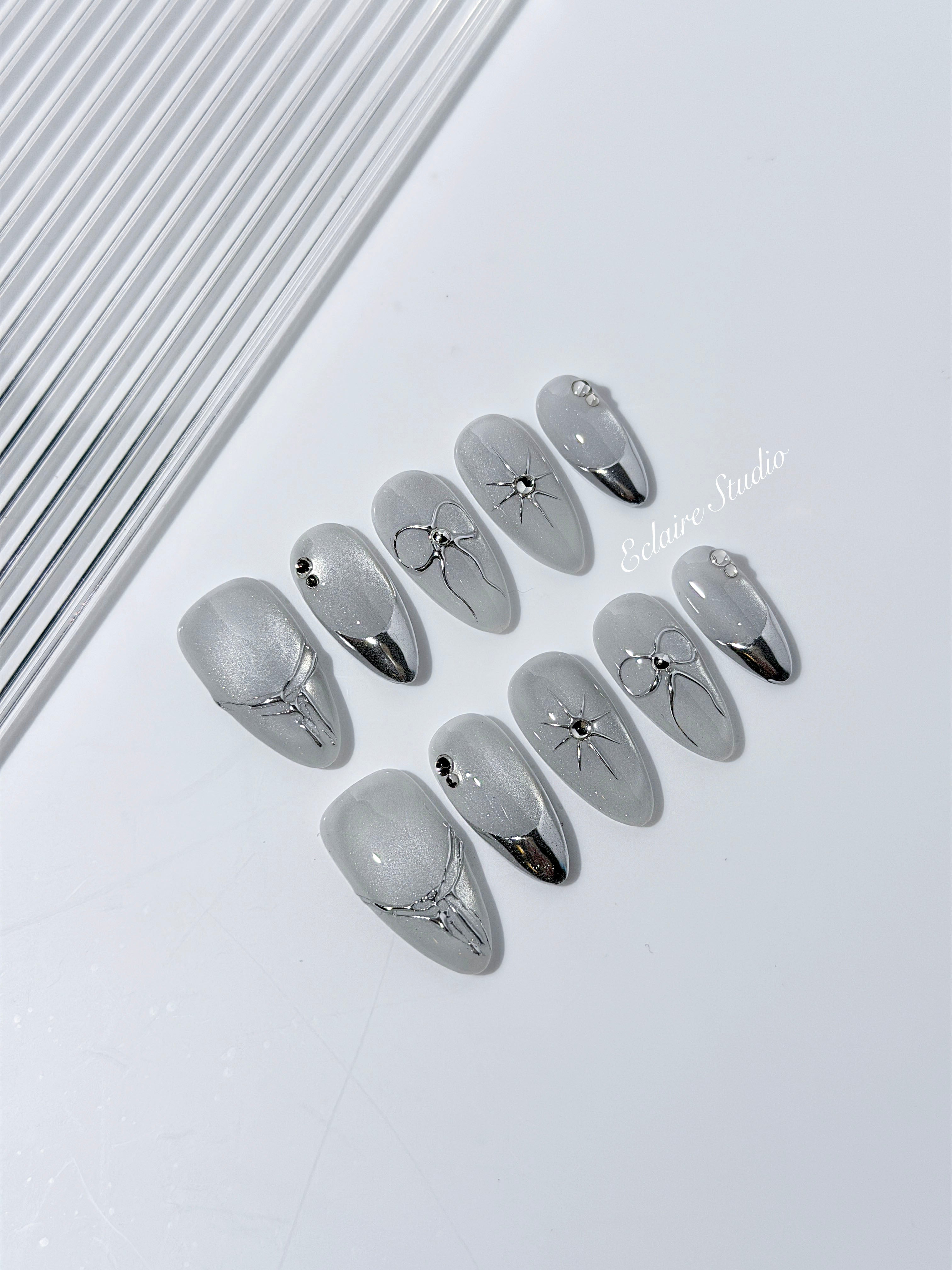 Silver cat-eye press-on nails featuring glazed chrome French tips and fine-line bow and starburst designs.