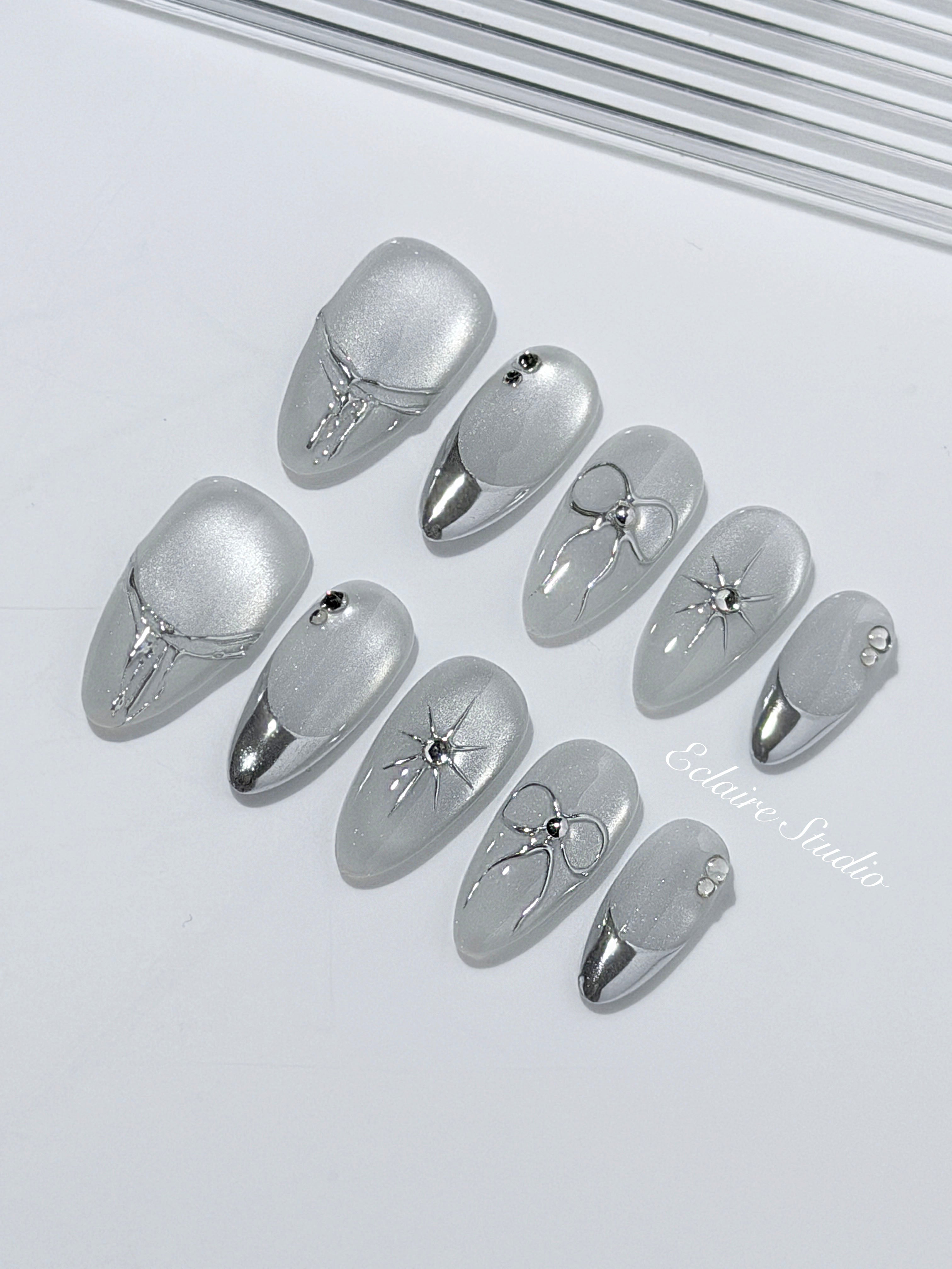 Silver cat-eye press-on nails featuring glazed chrome French tips and fine-line bow and starburst designs.