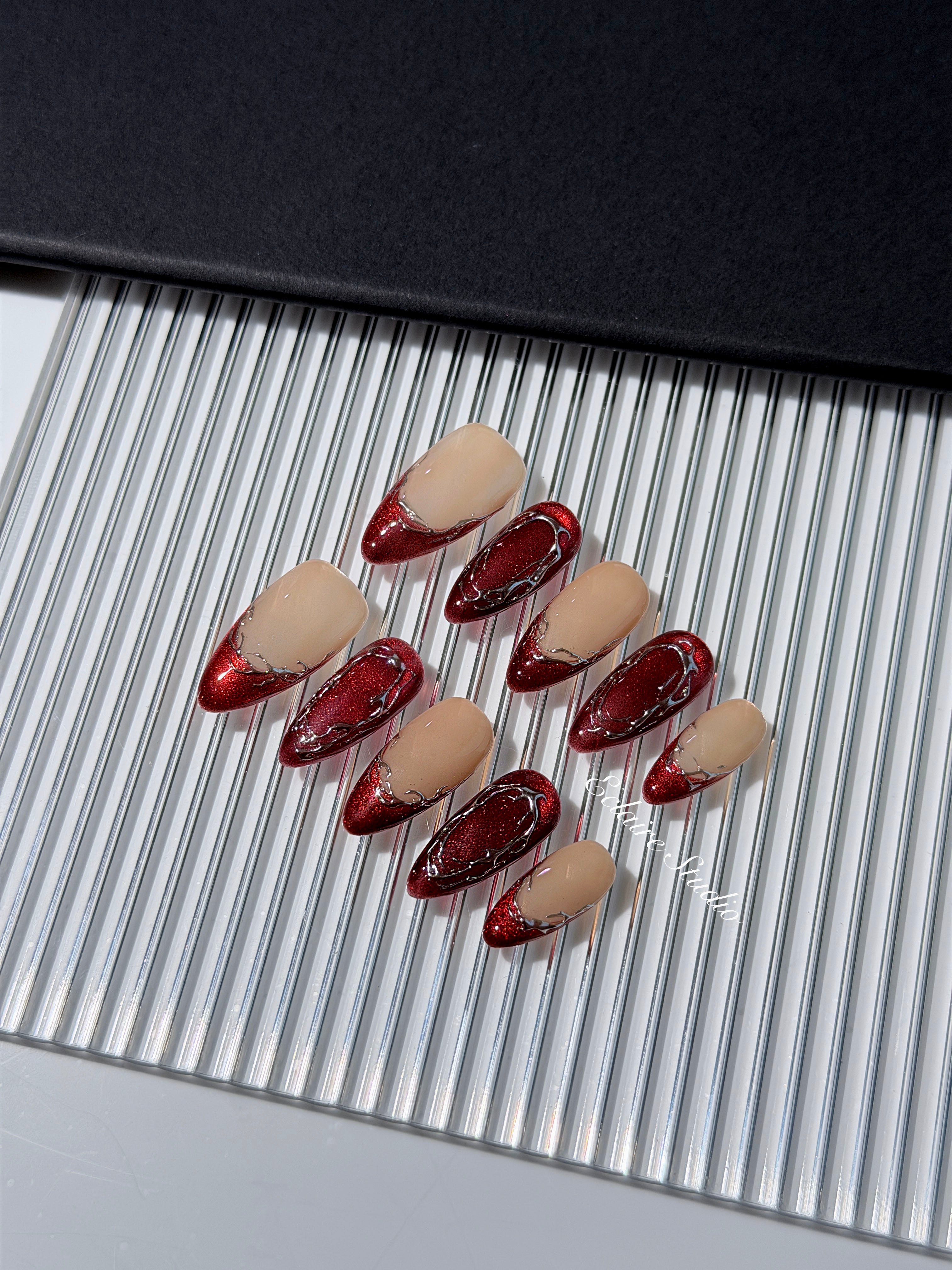 Red press-on nails with deep red cat-eye base, silver strokes, and nude contrast — Éclaire Nail Studio