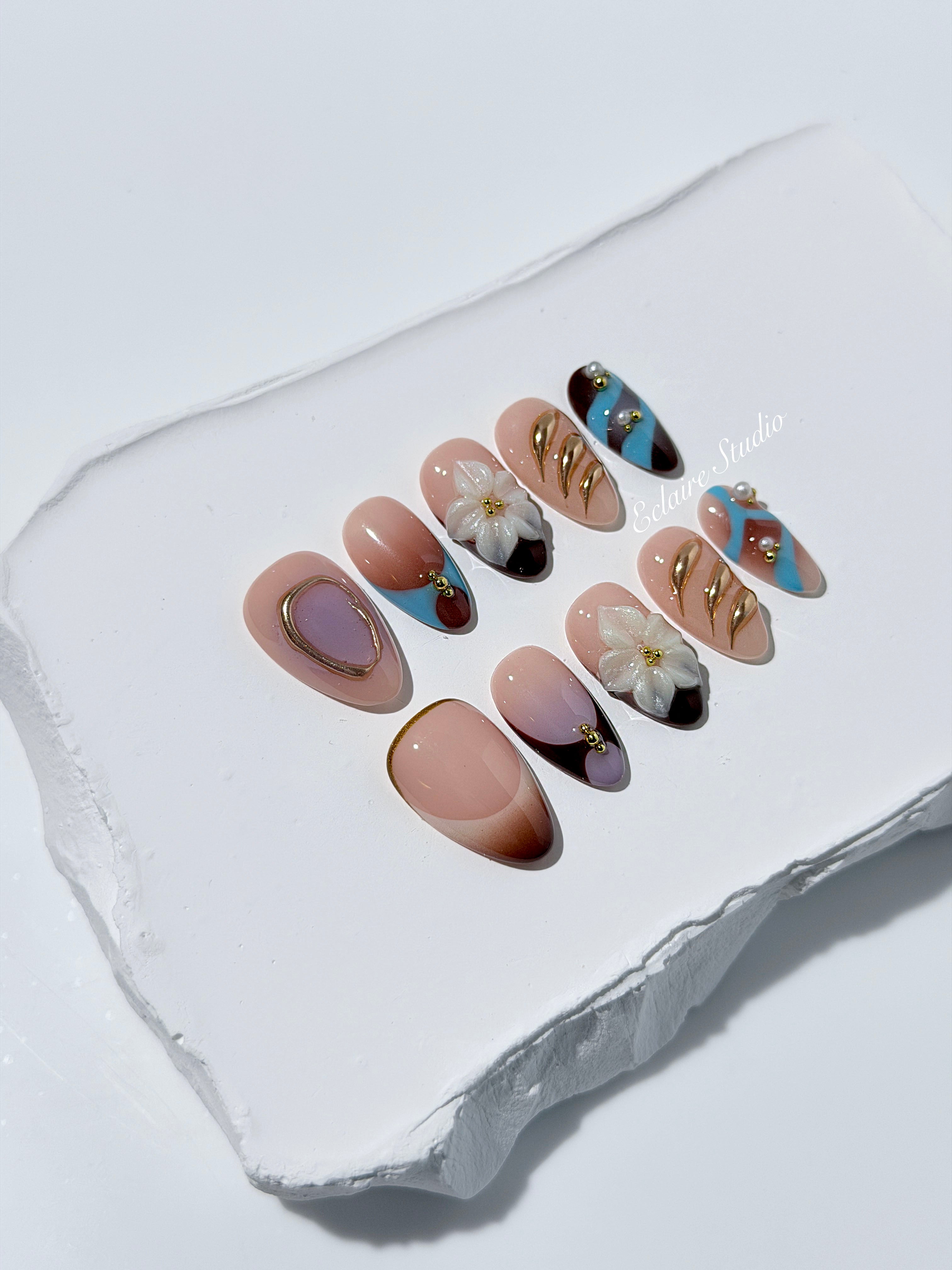 Warm gradient nails with gold trim, 3D white flowers, and blue accents inspired by the Nutcracker character