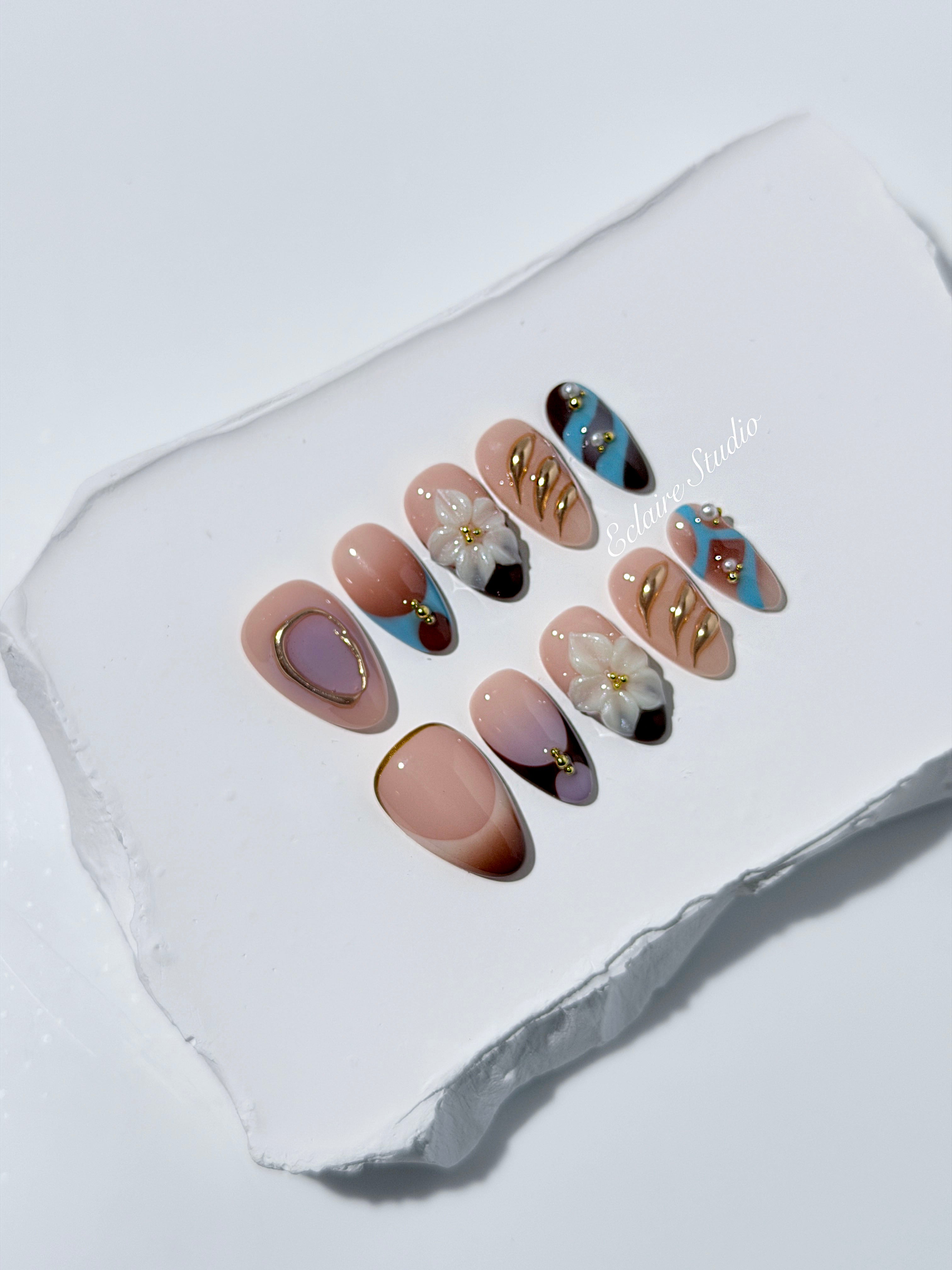 Warm gradient nails with gold trim, 3D white flowers, and blue accents inspired by the Nutcracker character