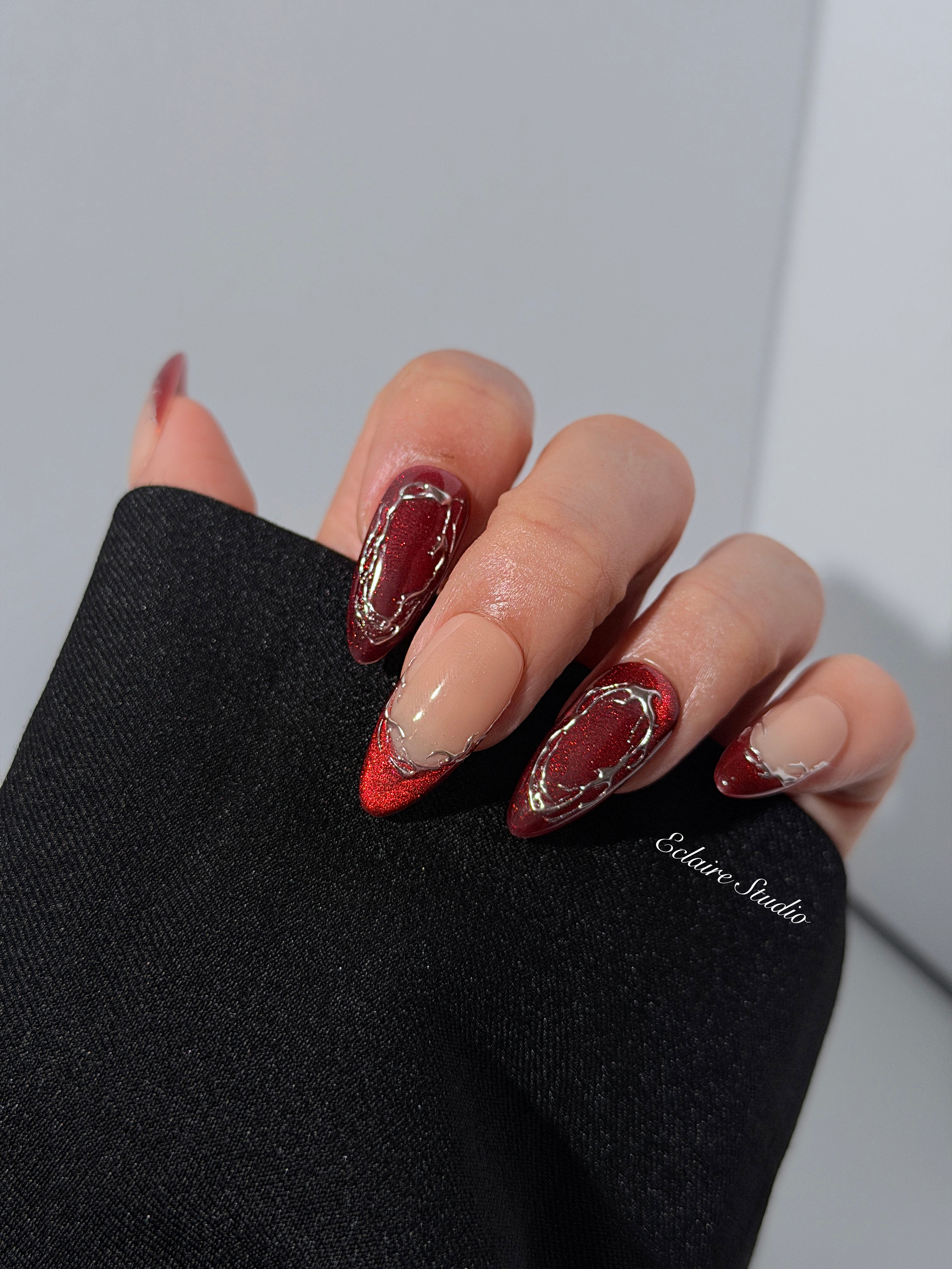Red press-on nails with deep red cat-eye base, silver strokes, and nude contrast — Éclaire Nail Studio