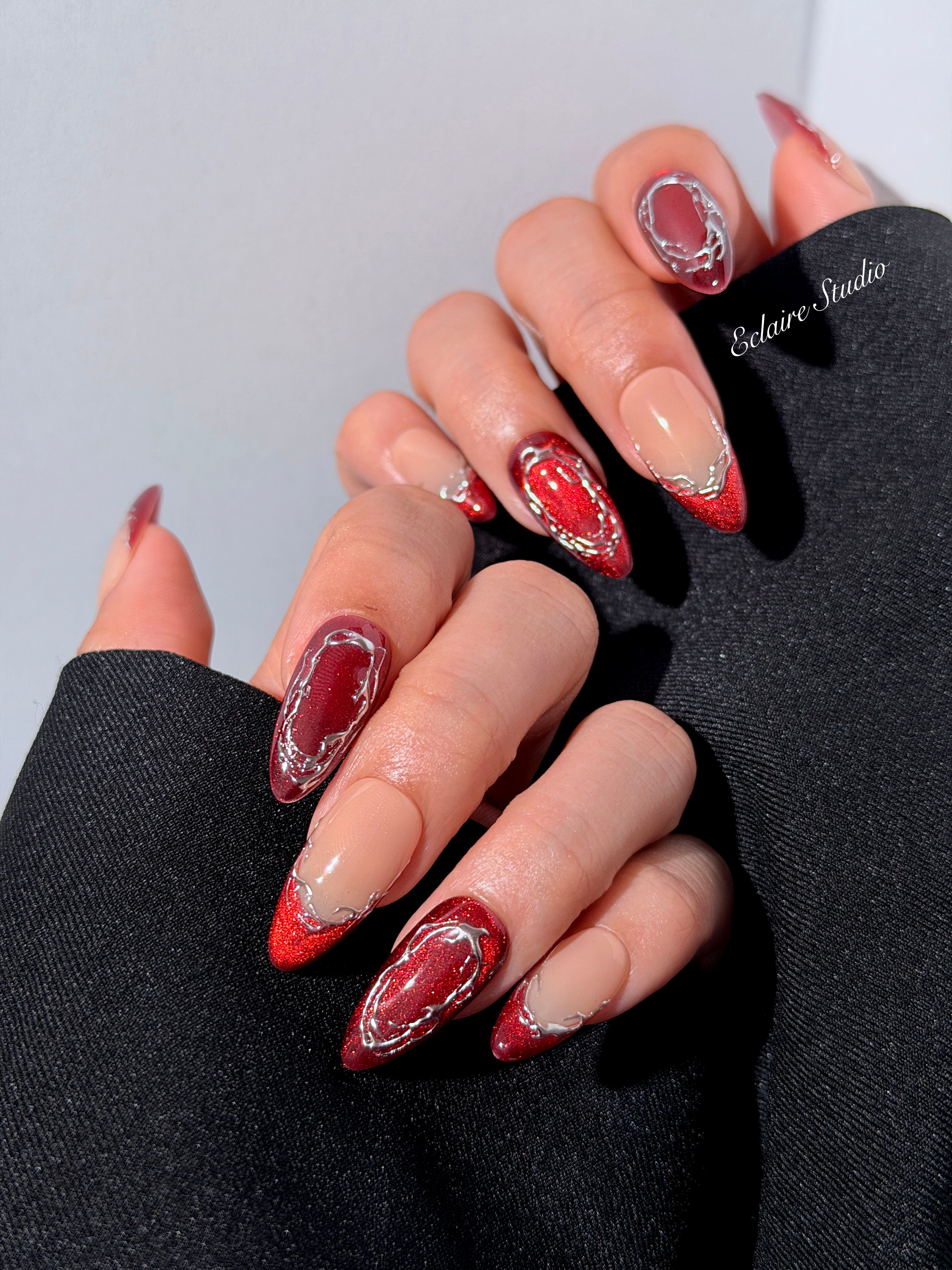 Red press-on nails with deep red cat-eye base, silver strokes, and nude contrast — Éclaire Nail Studio