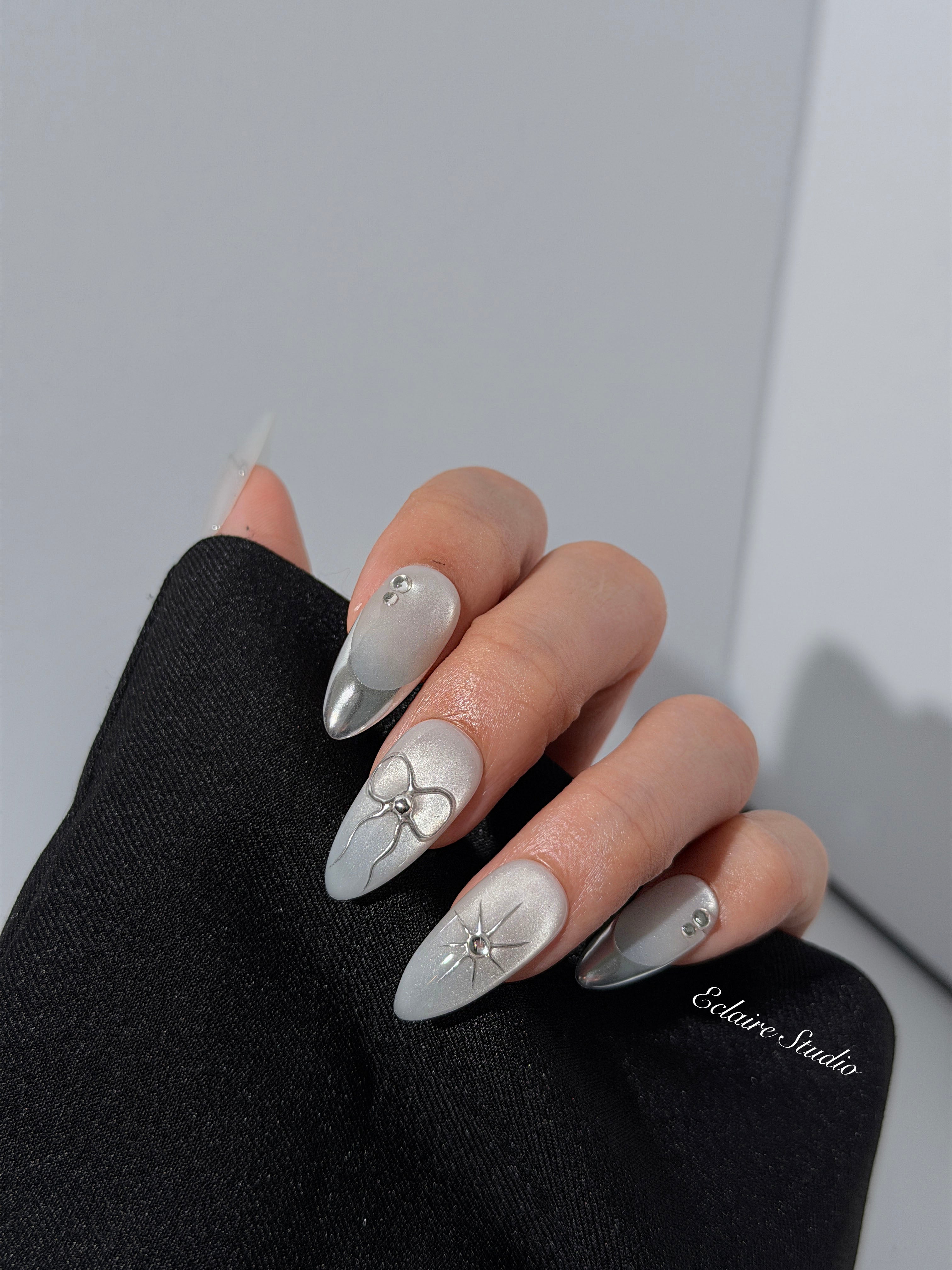 Silver cat-eye press-on nails featuring glazed chrome French tips and fine-line bow and starburst designs.