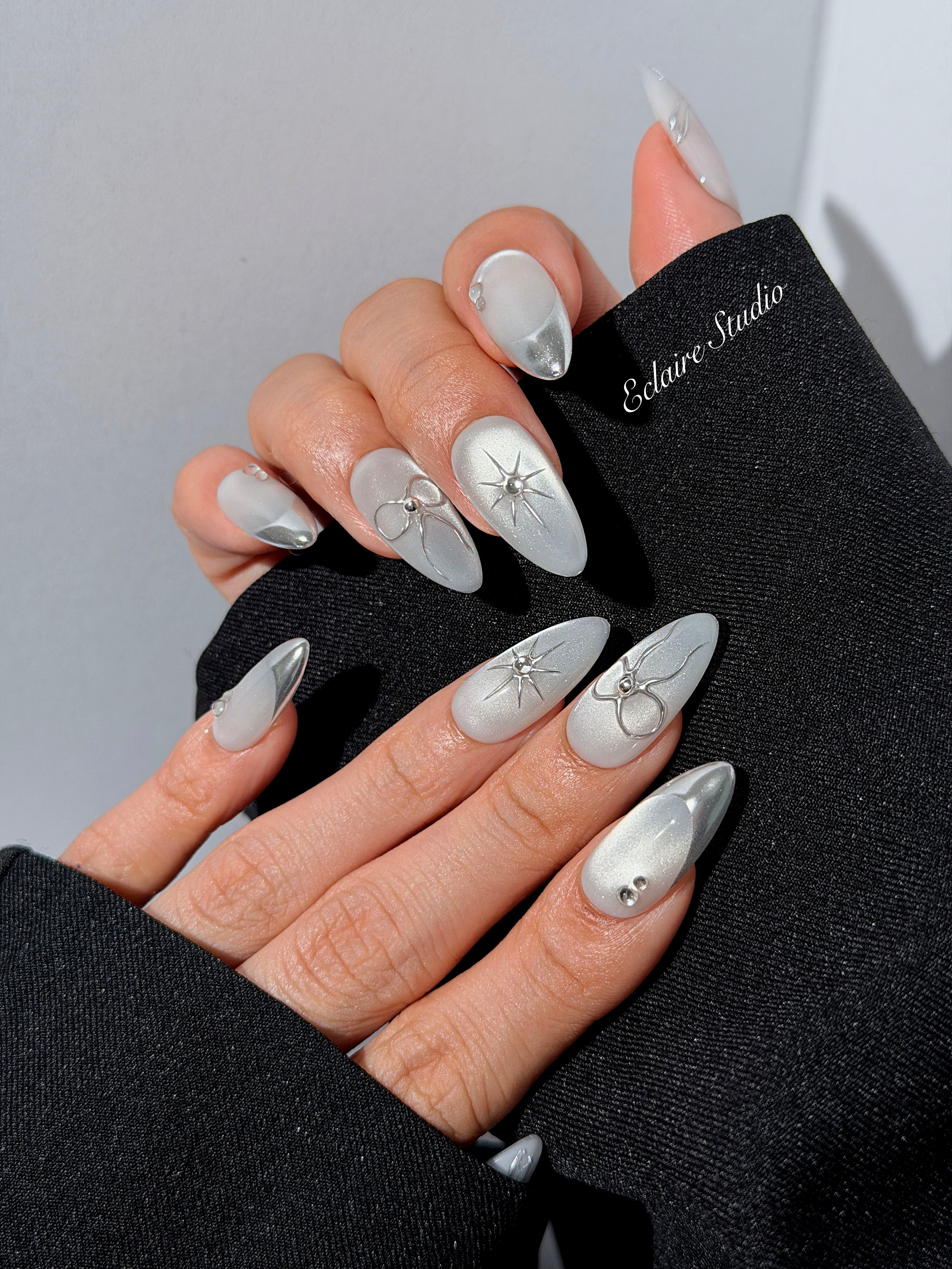 Silver cat-eye press-on nails featuring glazed chrome French tips and fine-line bow and starburst designs.