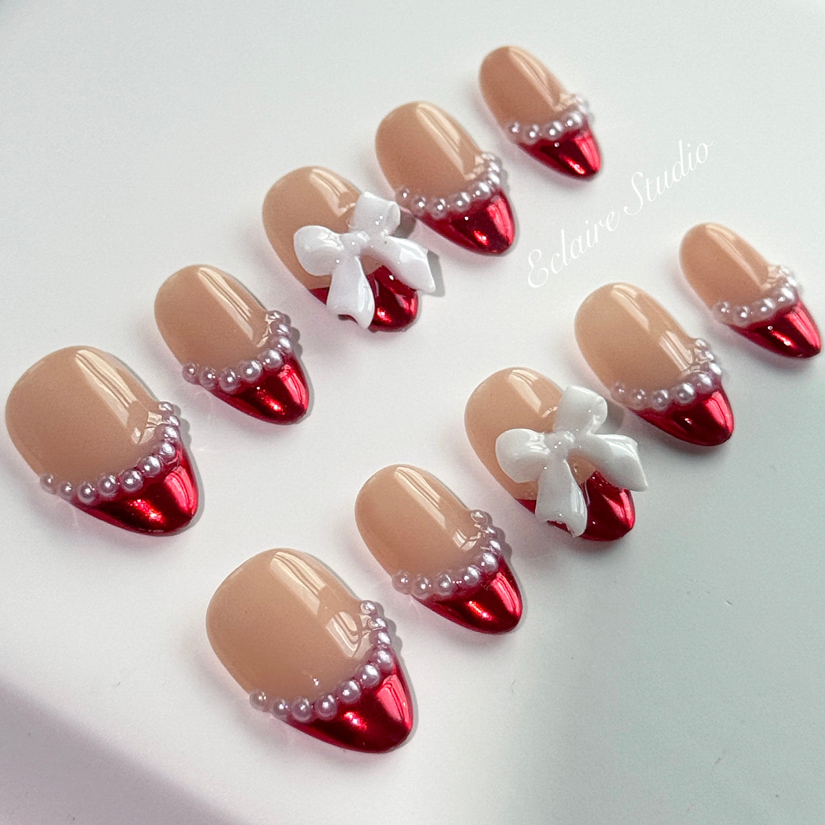 Red Ribbon press-on nails with glazed red chrome French tips, pearl trim, and 3D white bow accents.”