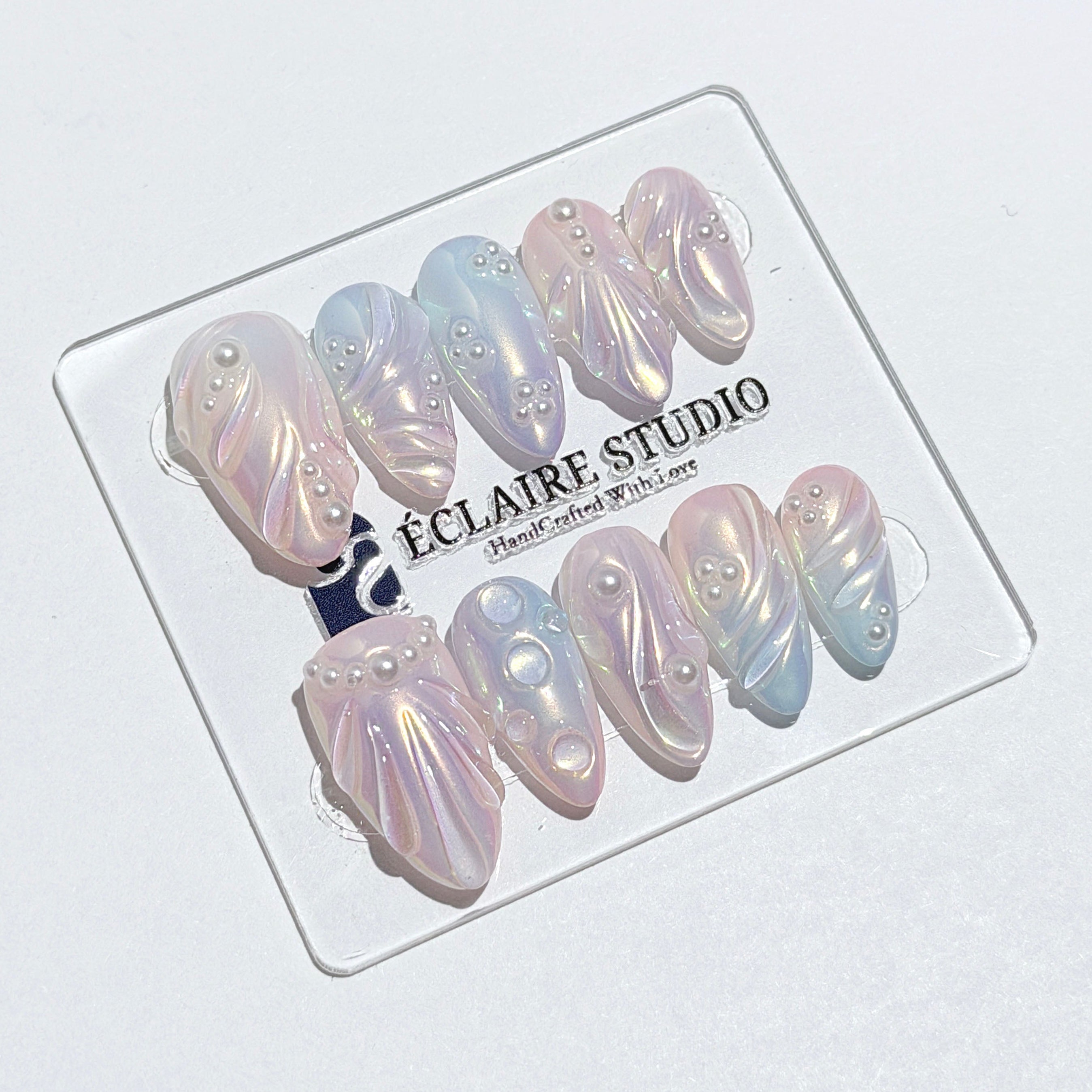 Handcrafted luxury press-on nails in a medium almond shape featuring an iridescent multi-toned glazed finish with 3D sculpted shell ridges and delicate mini pearls.