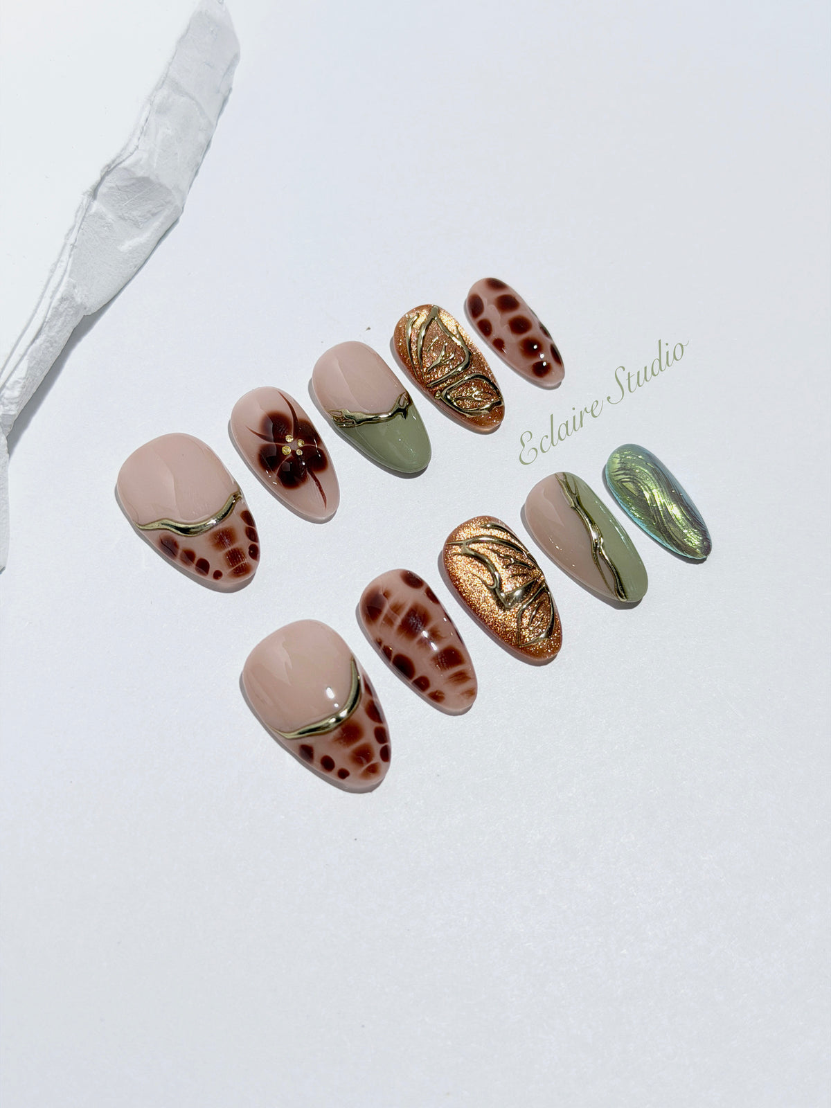 Olive Reverie short almond press-on nails with brown and green cat-eye shimmer, olive French tips, animal prints, floral art, and raised gold details.