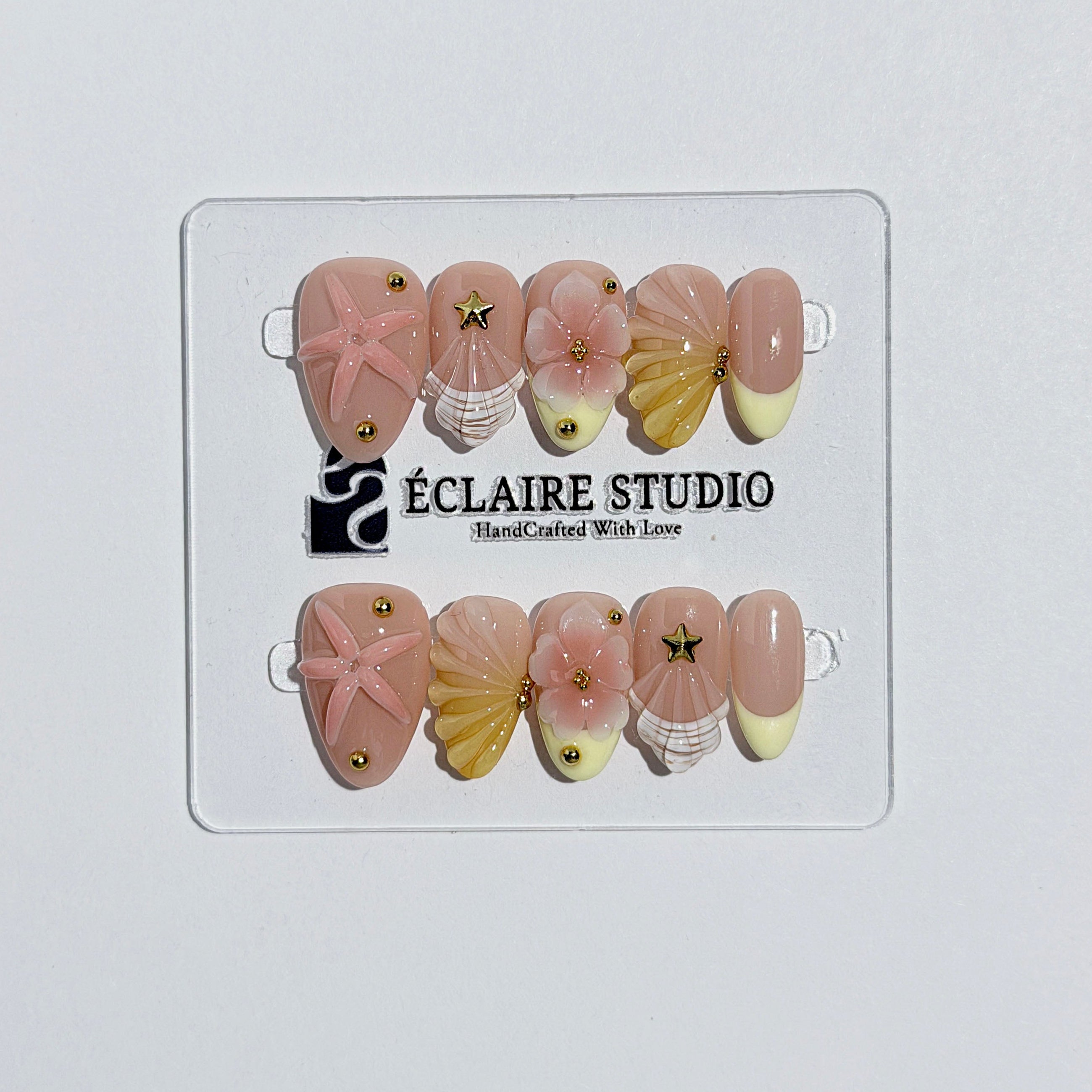 Summer Eclaire Nail Studio Luxury short almond press-on nails featuring a sheer nude base with butter yellow French tips, hand-sculpted 3D pink starfish, amber-tinted 3D seashells, and flowers with gold accents.