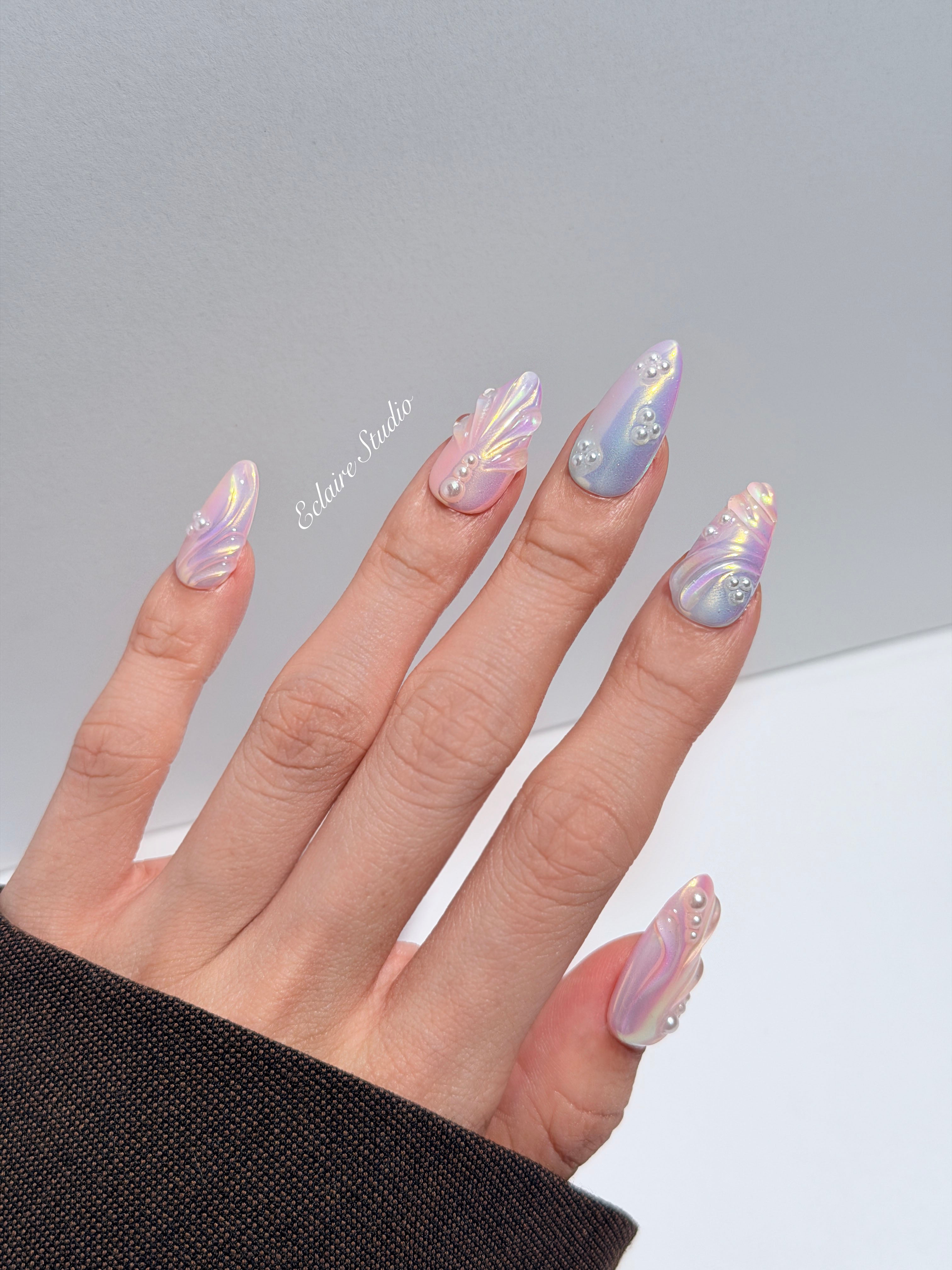 Handcrafted luxury press-on nails in a medium almond shape featuring an iridescent multi-toned glazed finish with 3D sculpted shell ridges and delicate mini pearls.