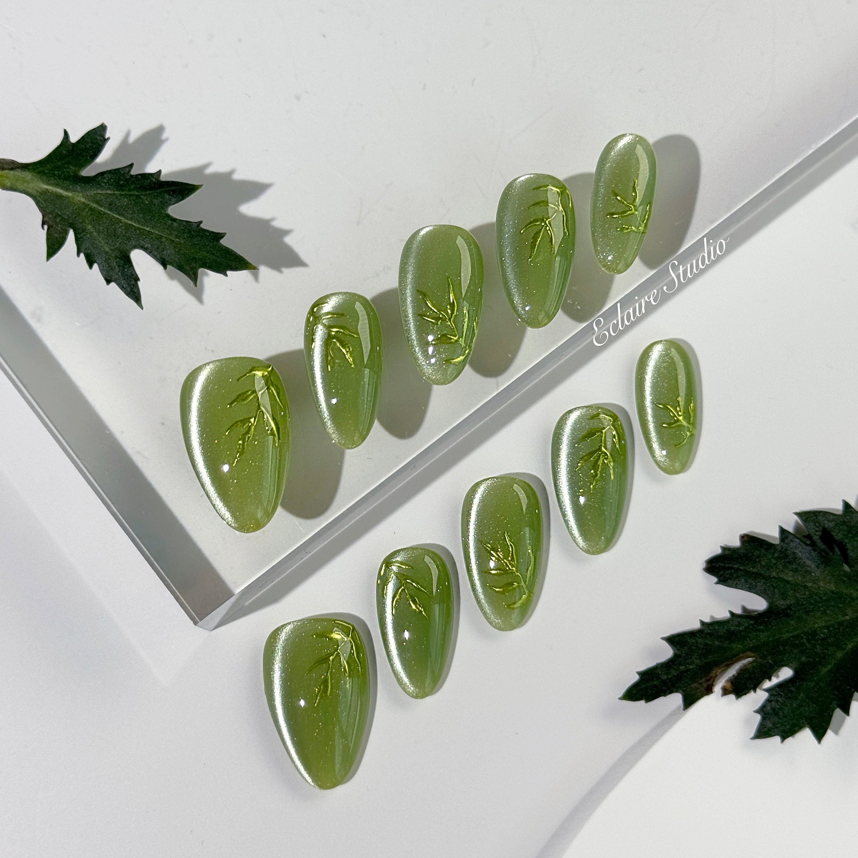 Green cat-eye press-on nails featuring layered ivy designs brushed with shiny green powder — Éclaire Nail Studio