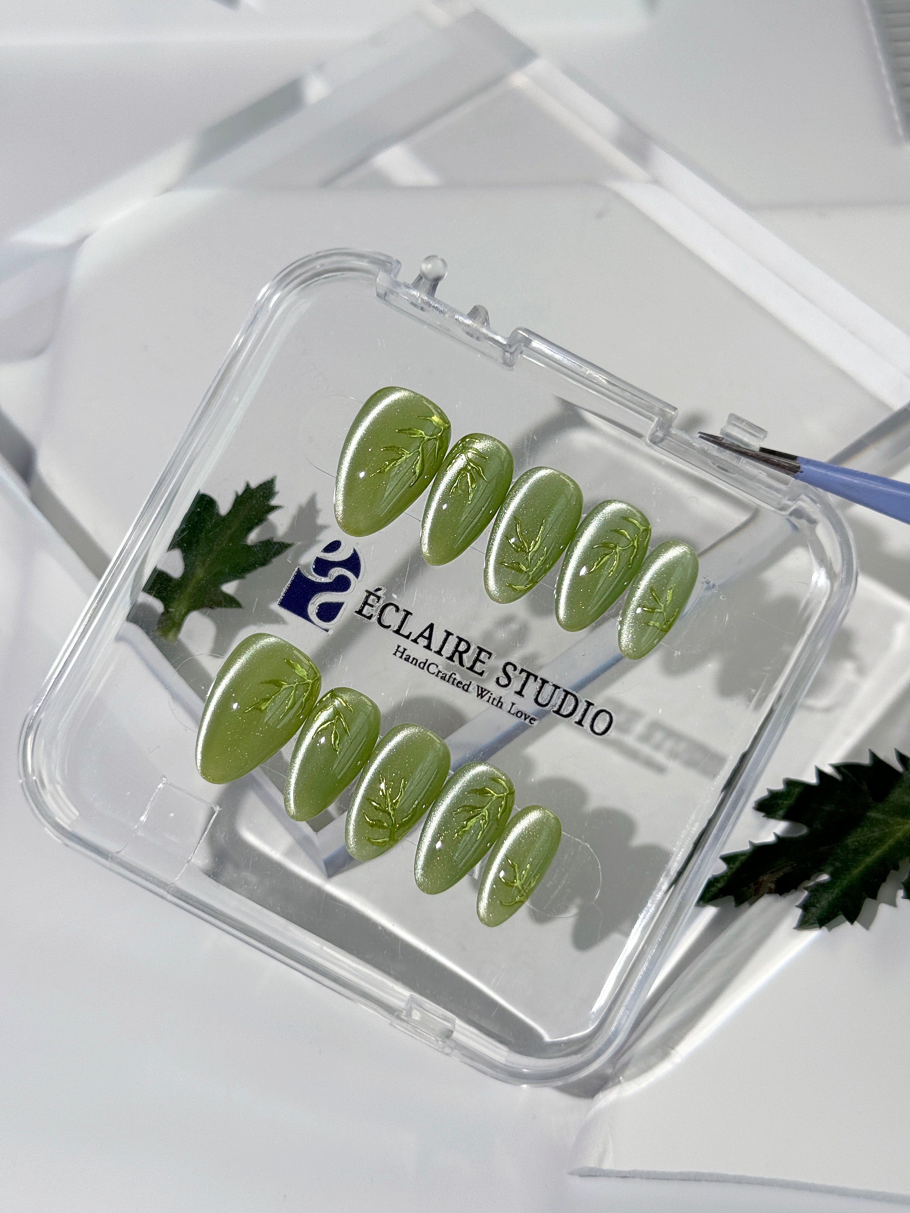 Green cat-eye press-on nails featuring layered ivy designs brushed with shiny green powder — Éclaire Nail Studio