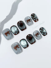 Short coffin press-on nails in mint and chocolate brown gradient with 3D heart and bow accents, displayed in a clear Éclaire Studio case under soft lighting.