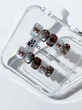 Short coffin press-on nails in mint and chocolate brown gradient with 3D heart and bow accents, displayed in a clear Éclaire Studio case under soft lighting.