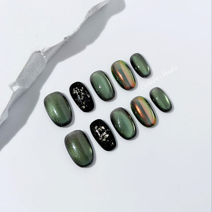 Short round press-on nails in shifting evergreen cat-eye shimmer with black and gold foil accent, displayed in a clear Éclaire Studio case.