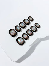 Short squoval press-on nails with dark brown base and iridescent frosted shimmer center, styled on white stone background.