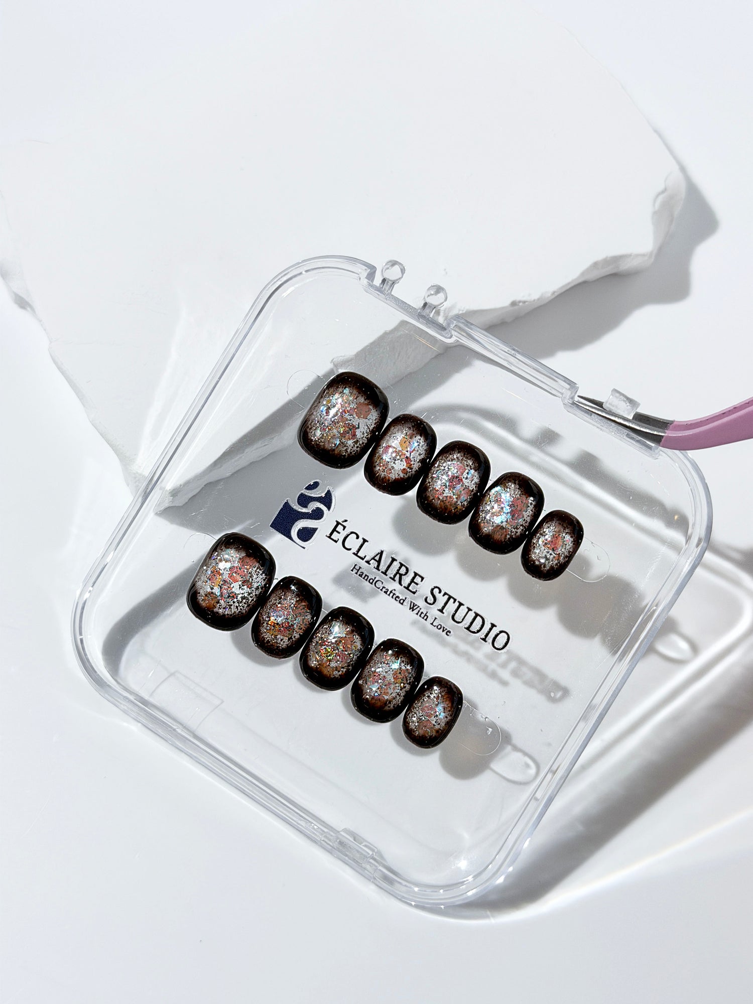 Short squoval press-on nails with dark brown base and iridescent frosted shimmer center, styled on white stone background.