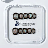 Short squoval press-on nails with dark brown base and iridescent frosted shimmer center, styled on white stone background.