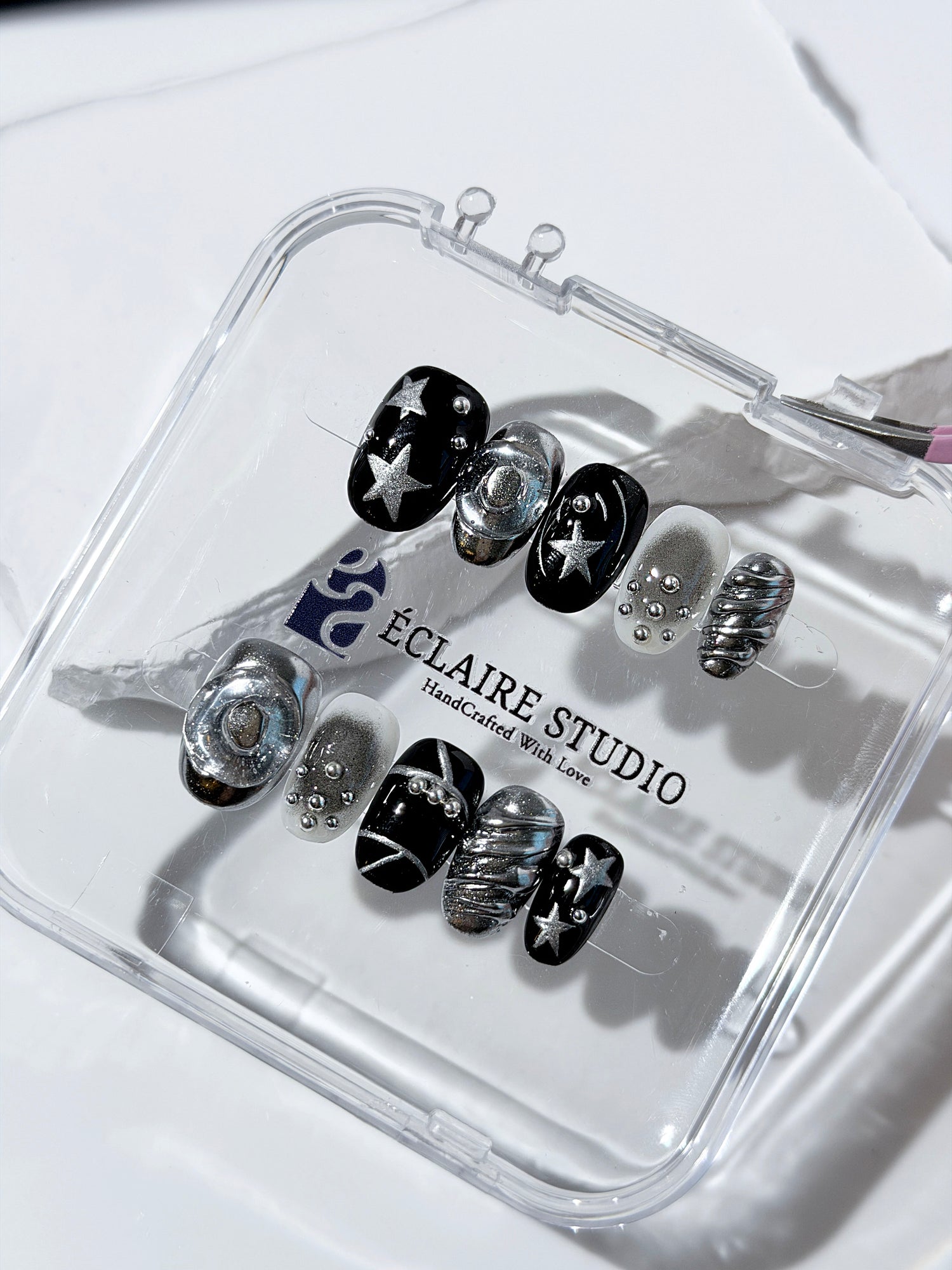 Black and silver press-on nails with 3D chrome swirl accents, star details, and shimmer gradient in a bold winter aesthetic.
